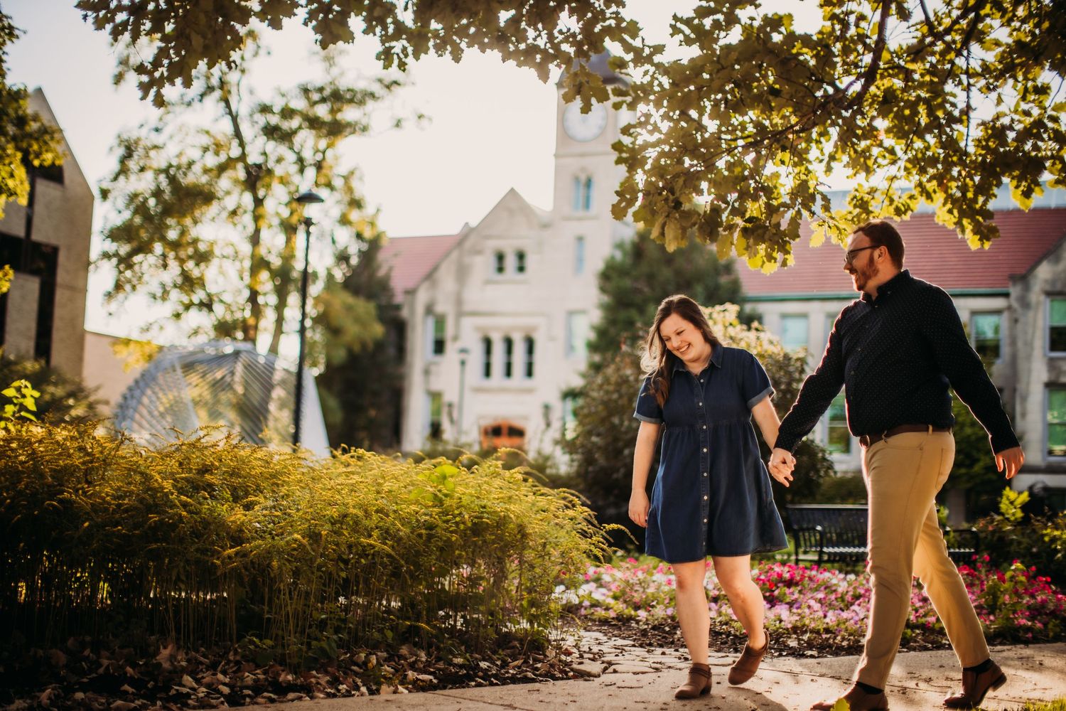 Tender embrace captured in warm evening sunlight with trees and buildings in background.