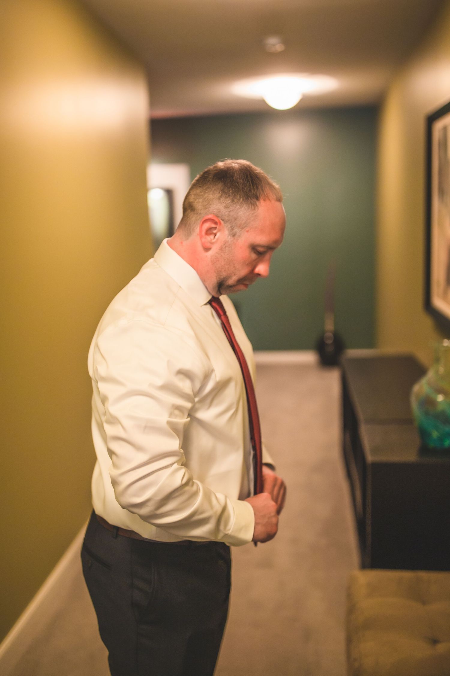 Person in white dress shirt and red tie stands in a hallway with olive green walls.