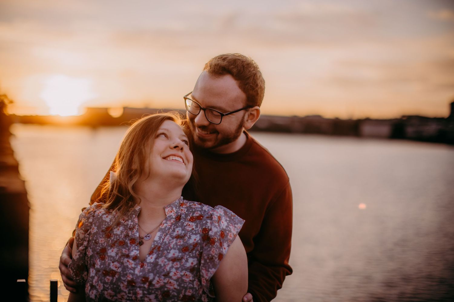 Romantic waterfront photoshoot with couple laughing during golden hour.