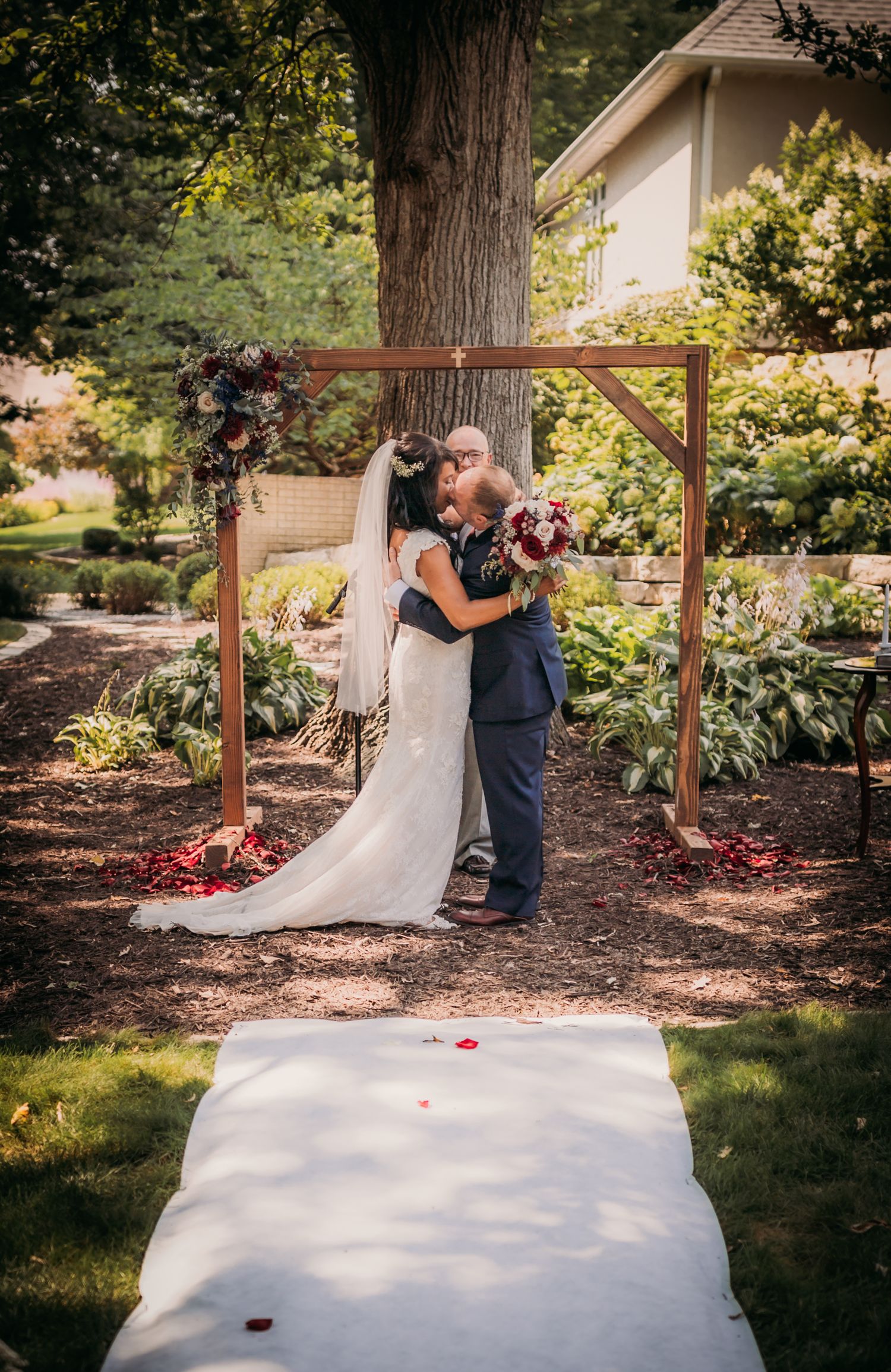 A couple shares a romantic moment under a wooden arch in a garden wedding setting.