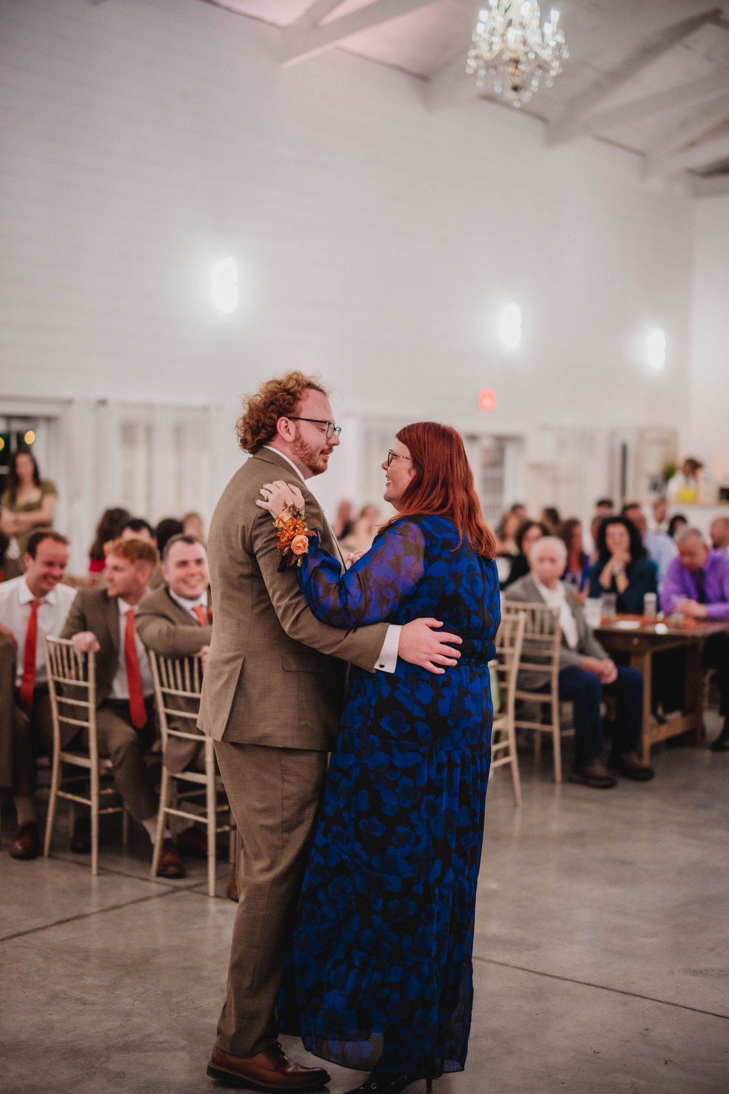 Two people dance together at a wedding reception while guests look on from their seats.