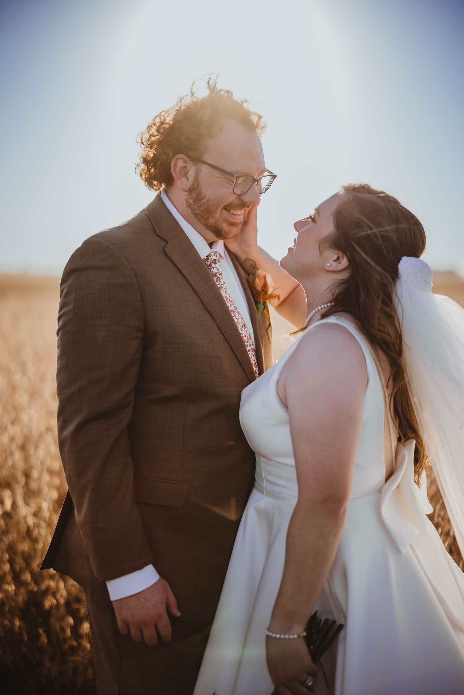 Intimate wedding portrait of couple sharing a tender moment in a sun-lit field.