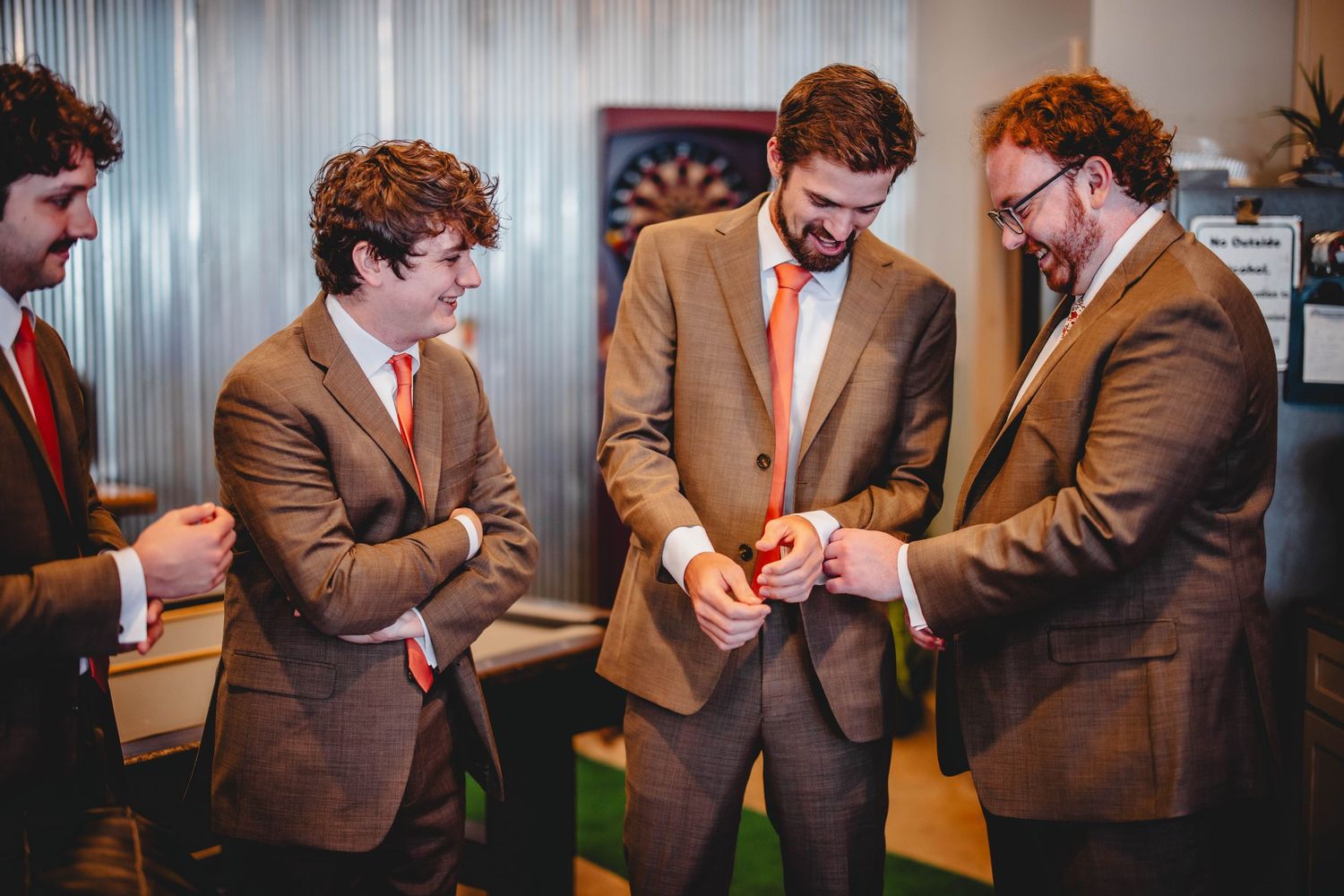 A group in matching brown suits gather to examine something in their hands.