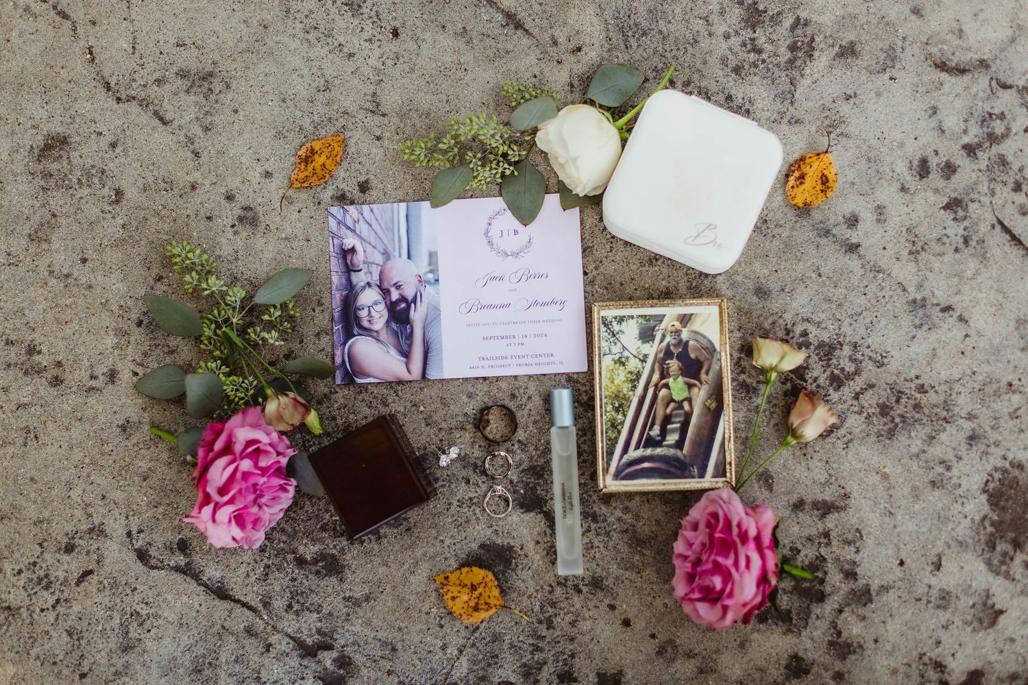 Wedding details flat lay with rings, roses, and invitation cards on concrete background.