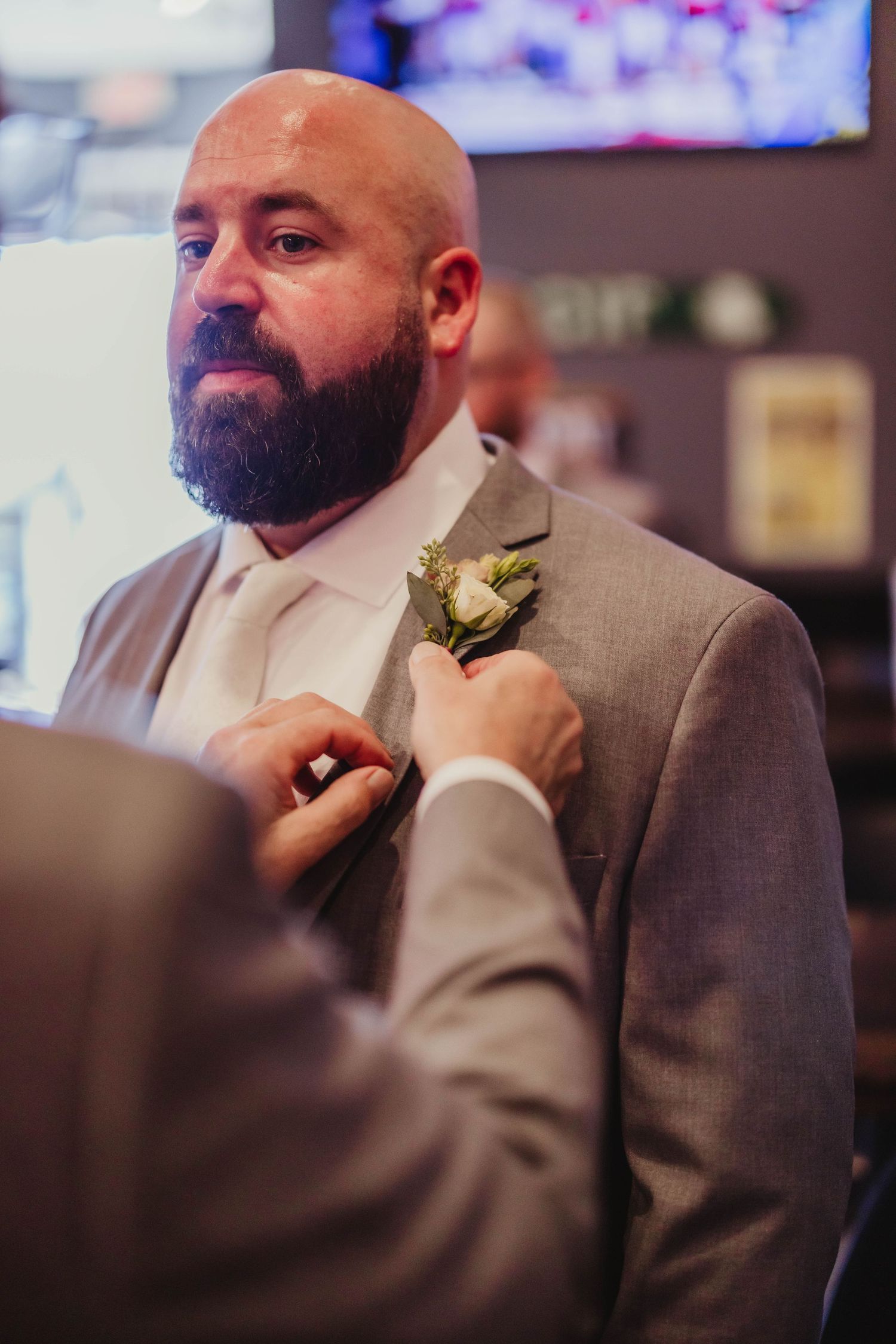 A boutonniere is being pinned onto a man's light grey suit jacket at a formal event.