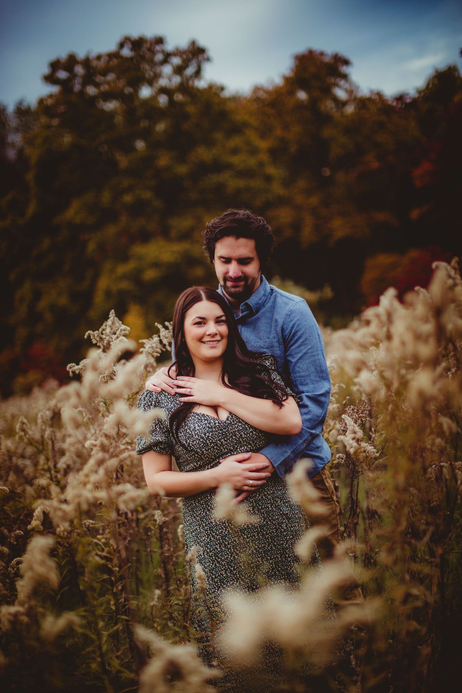 Romantic couple sharing intimate moment among wild grasses at sunset.