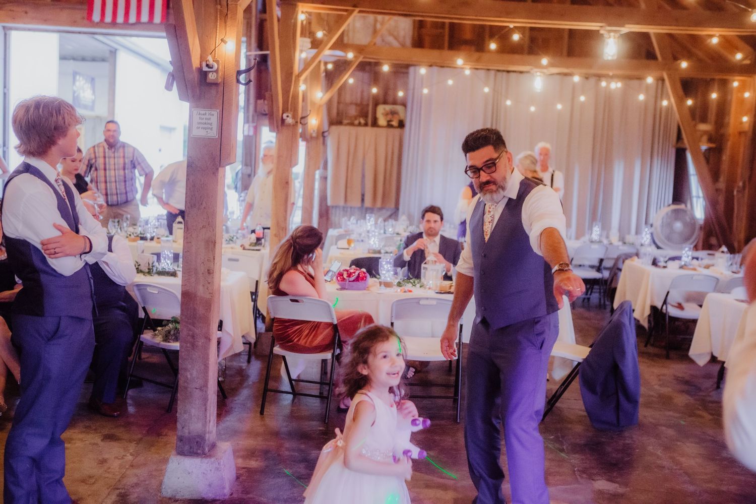 Wedding celebration inside a rustic barn venue decorated with twinkling lights and wooden beams.