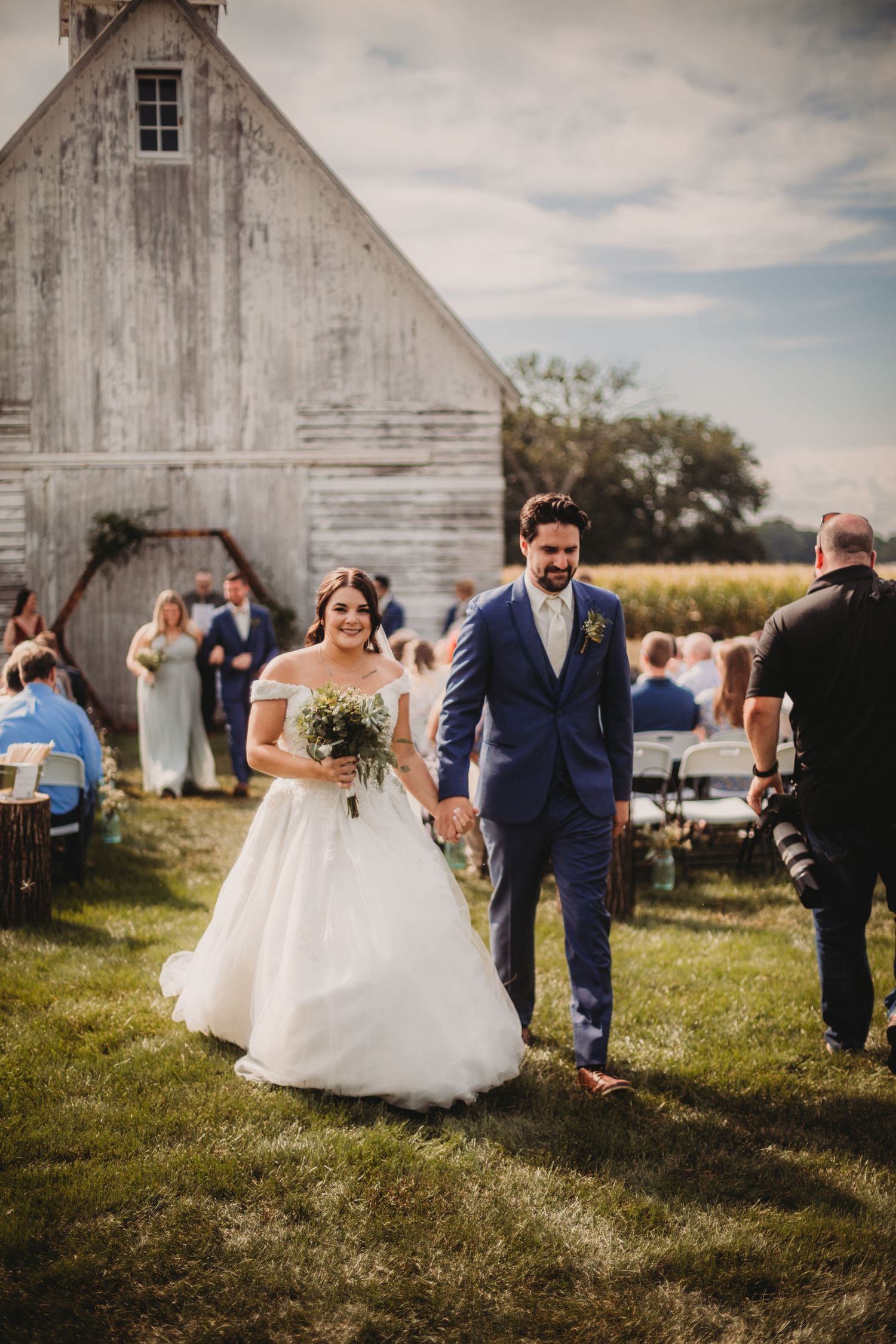 Guests celebrate at a rustic outdoor barn wedding with a white rustic barn backdrop in the countryside.