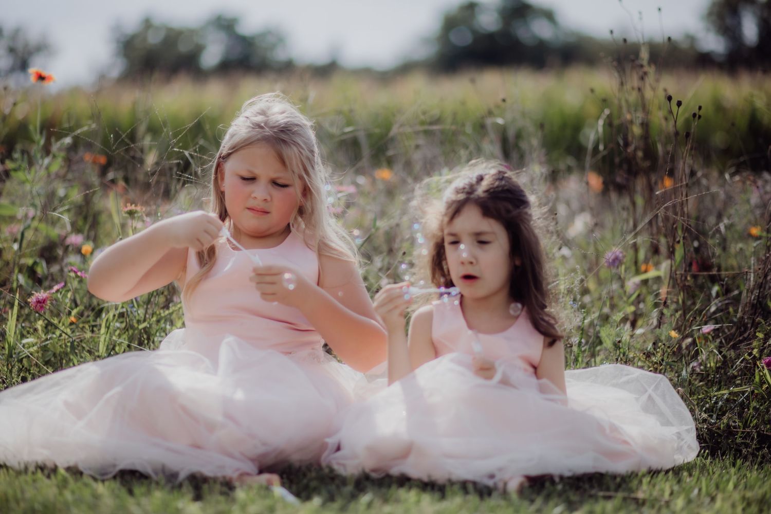 Young flower girls in white dresses play in a wildflower field.