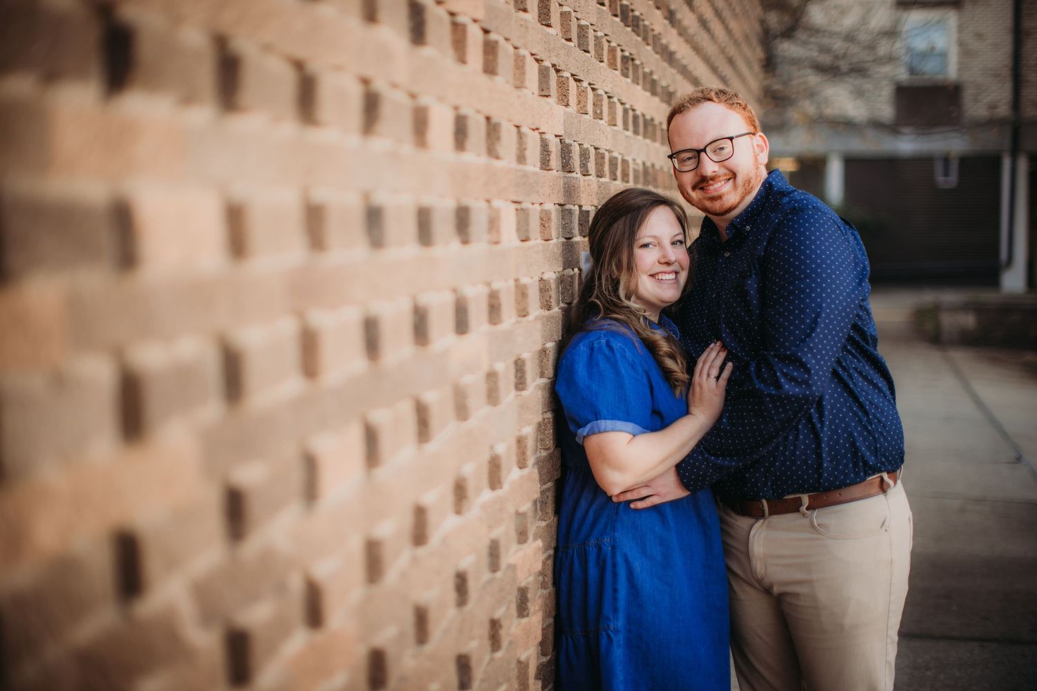 Happy couple laughing and embracing by a patterned brick wall.