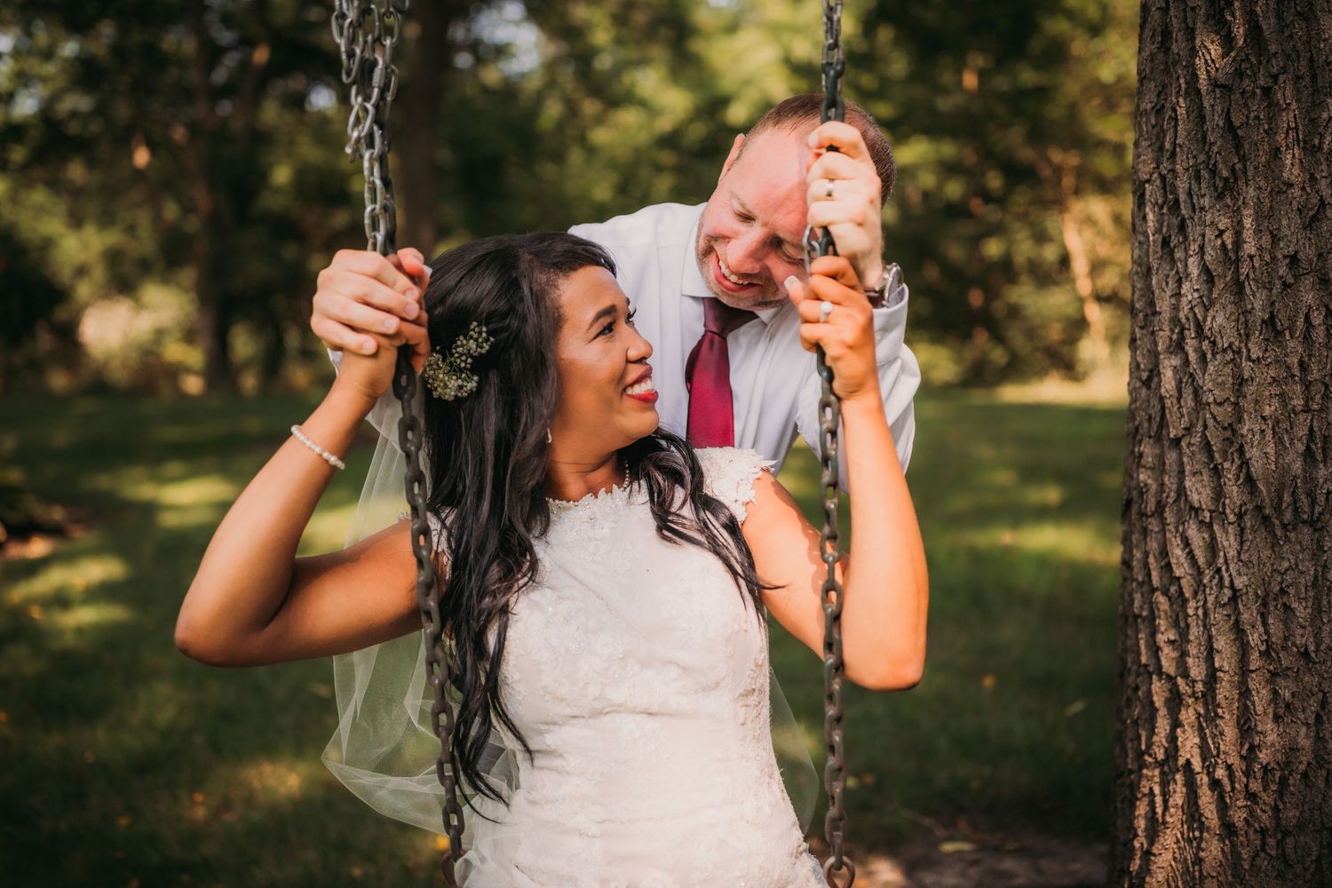 Candid moments of laughter between newlyweds on a swing in natural outdoor setting.