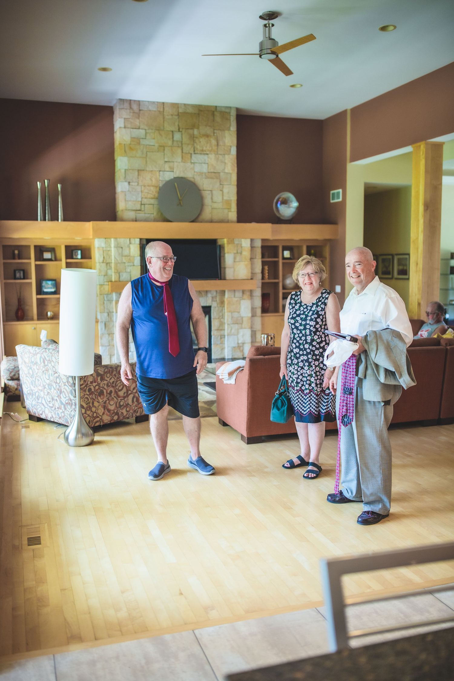 Group of people gather in a modern living room with stone fireplace and wooden floors.