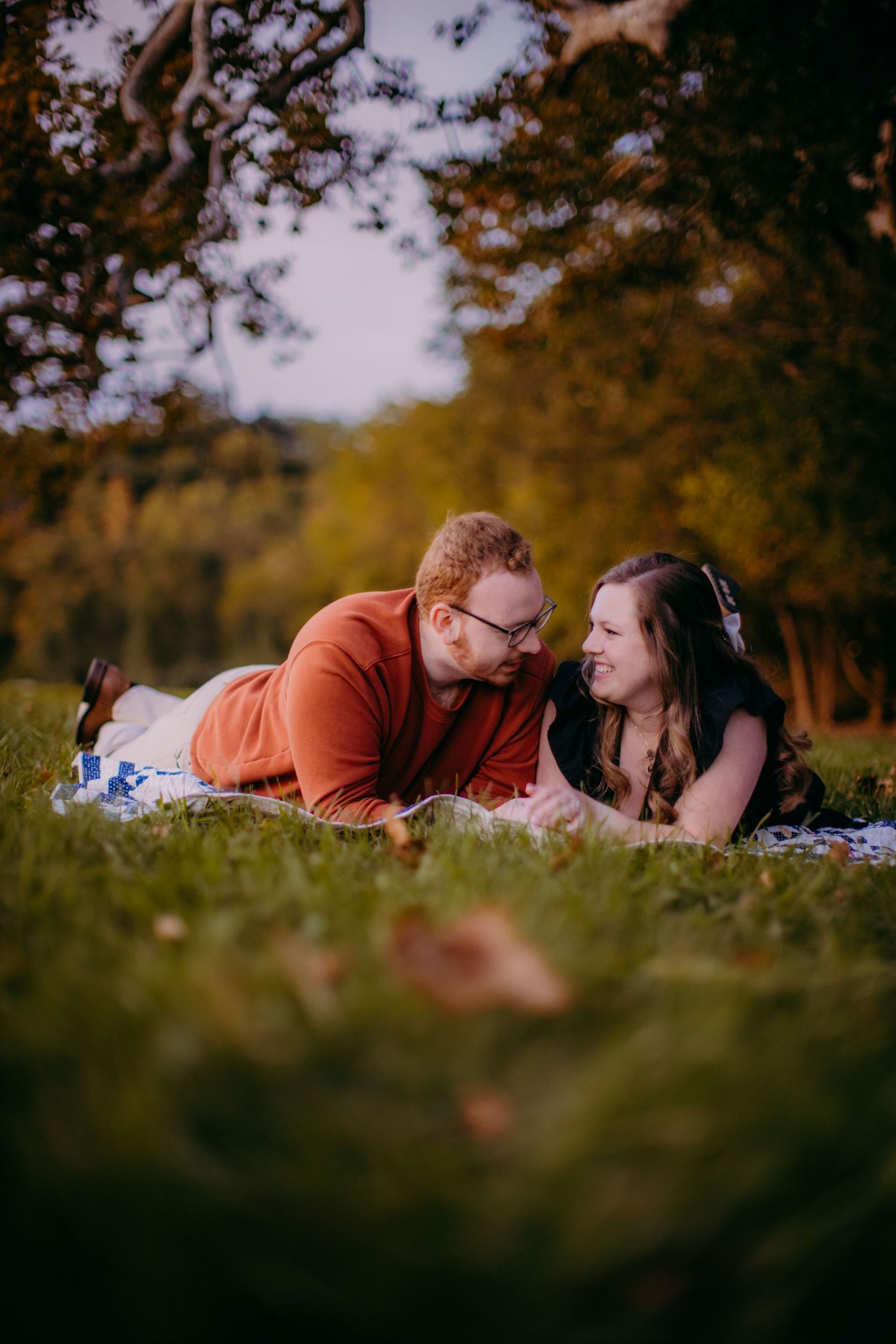 Couple sharing joyful moment while lying on blanket during fall photoshoot.