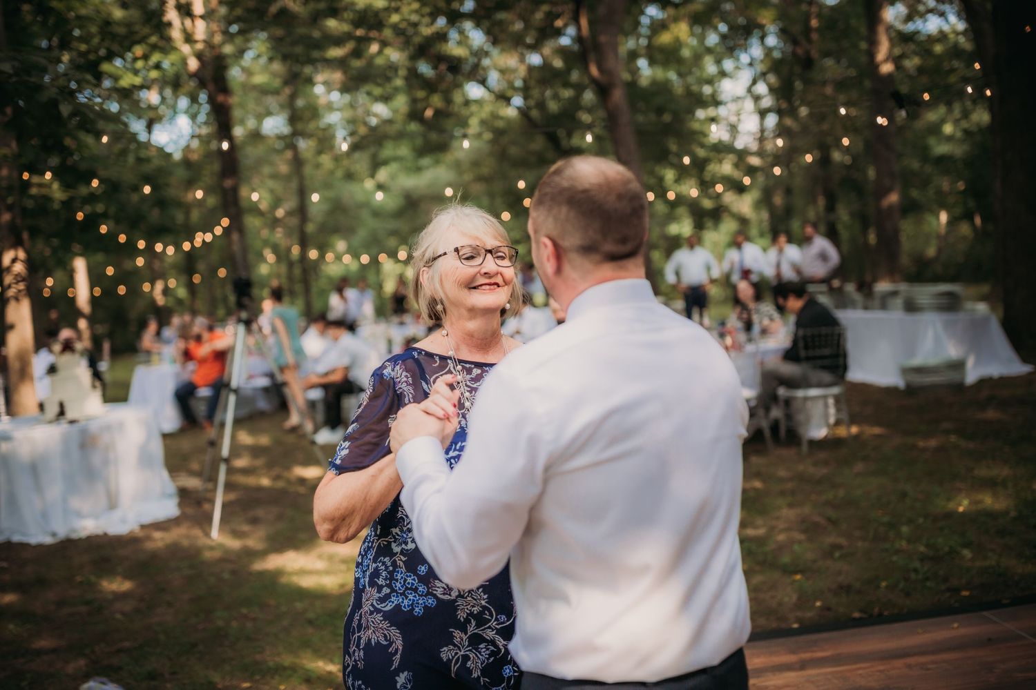 Joyful dance moment captured at outdoor wedding reception with string lights and forest backdrop.