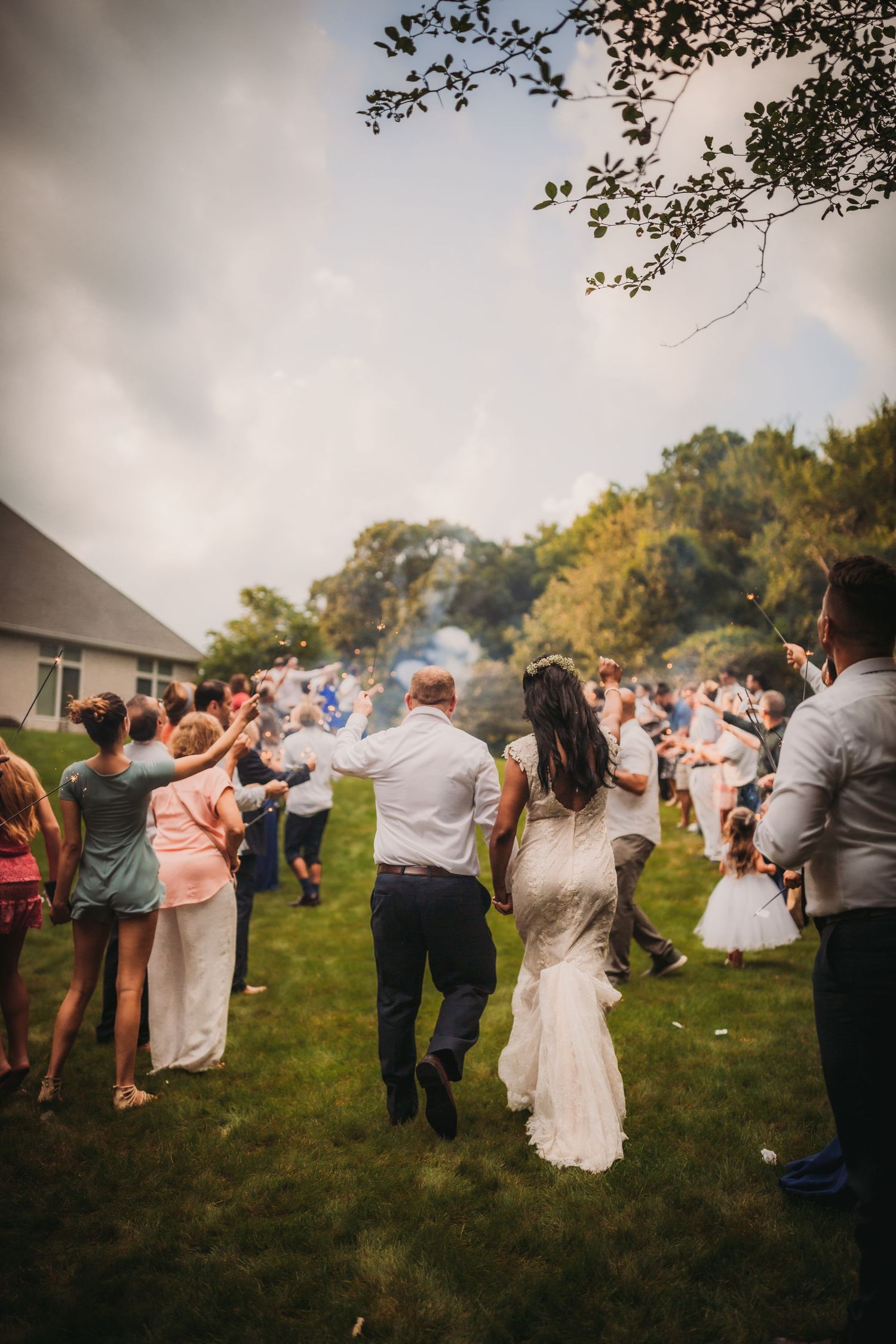 Wedding guests dancing on lawn with house and trees in background.