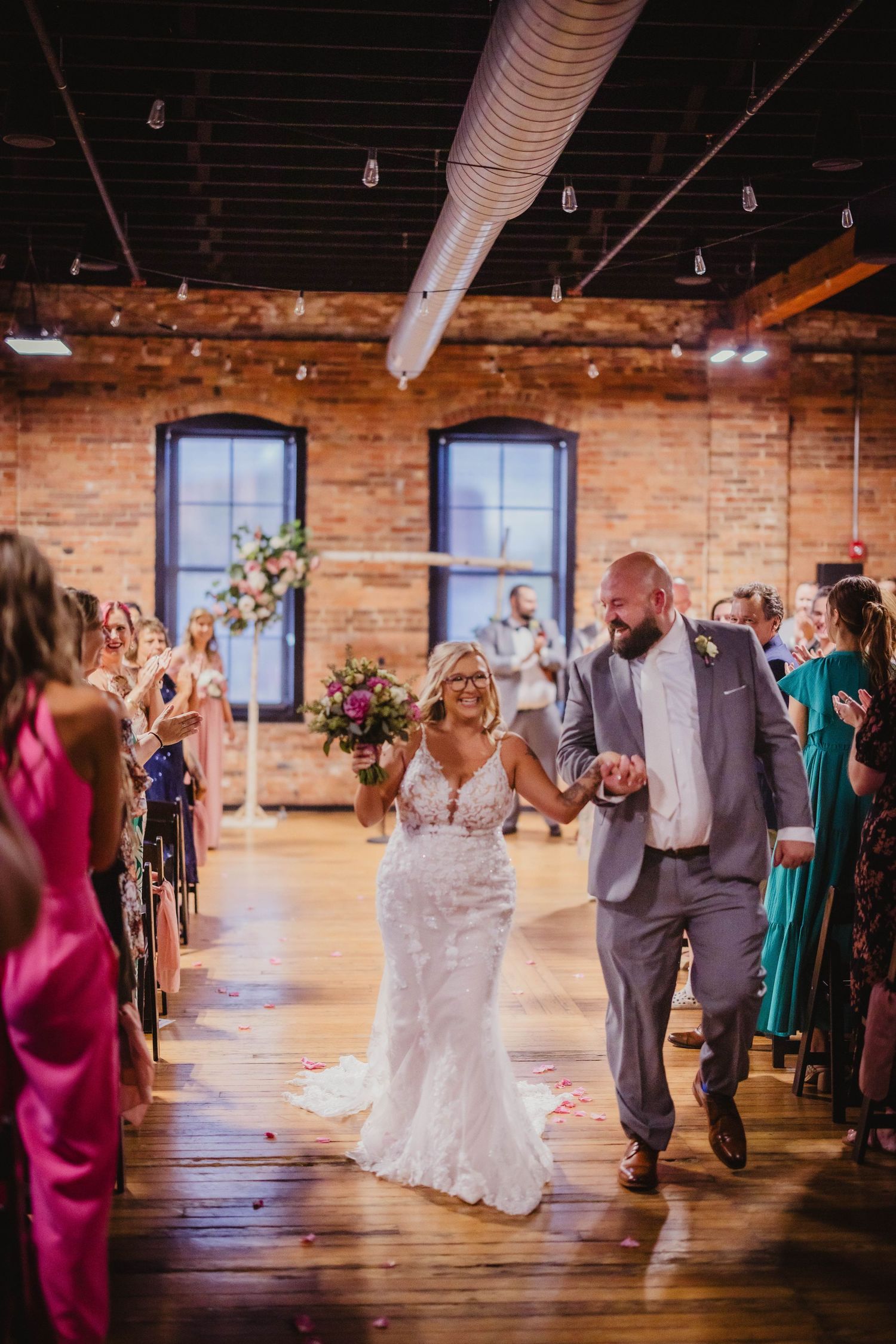 Wedding celebration in industrial venue as couple walks aisle between guests wearing vibrant dresses.