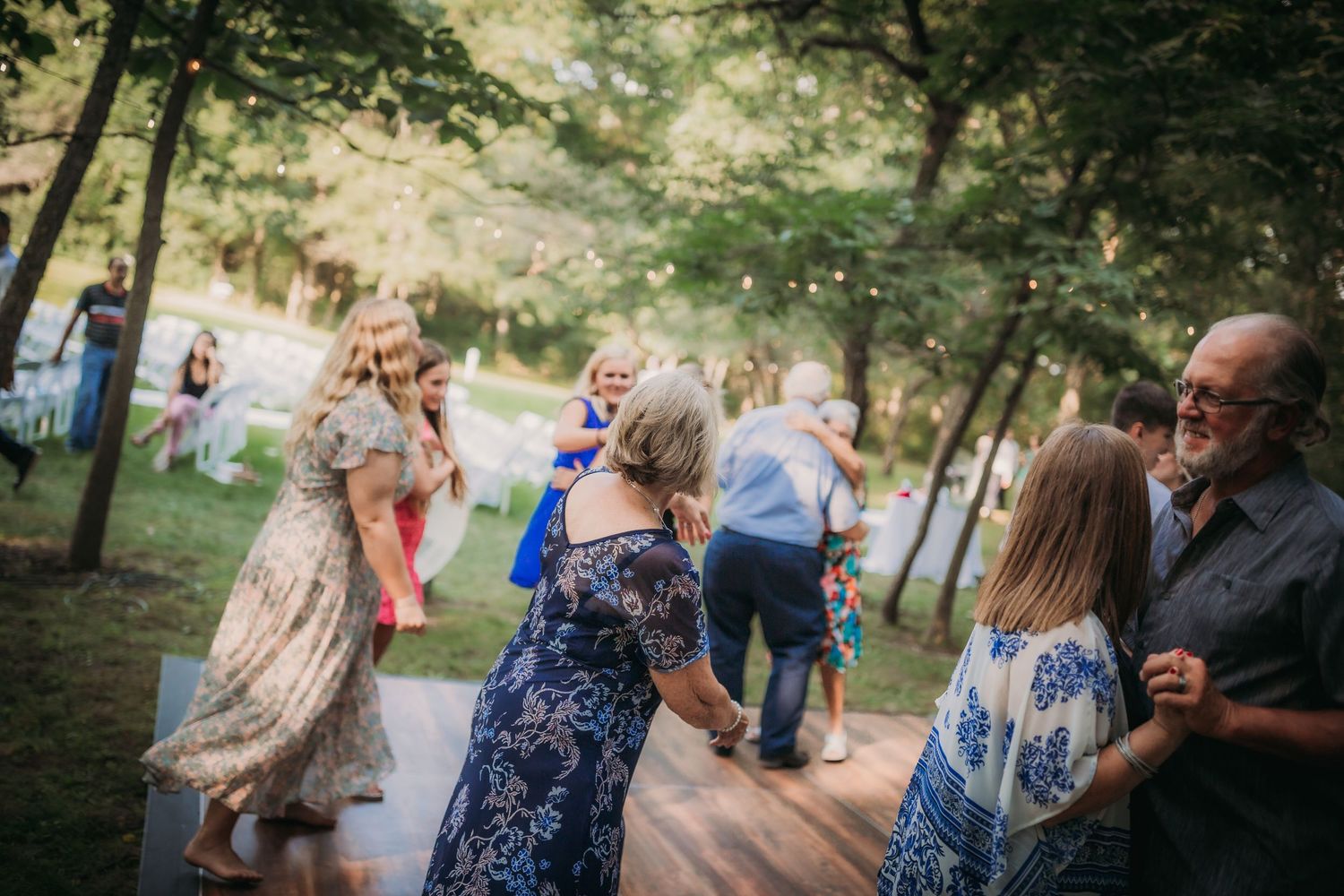 Wedding guests dancing on wooden platform at outdoor forest reception.