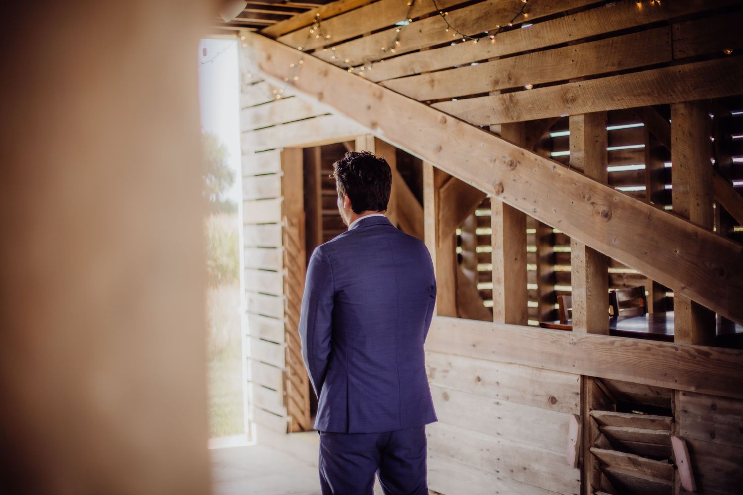 A wedding first look moment in a rustic barn with wooden walls and romantic string lights.