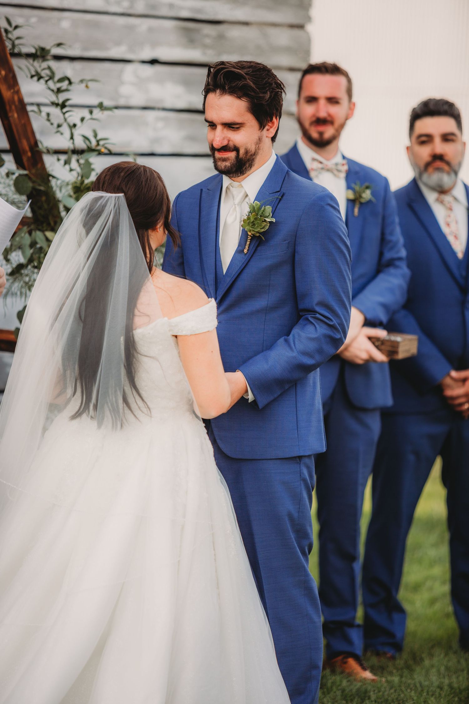 Wedding party in coordinated blue suits stands in line during outdoor ceremony.