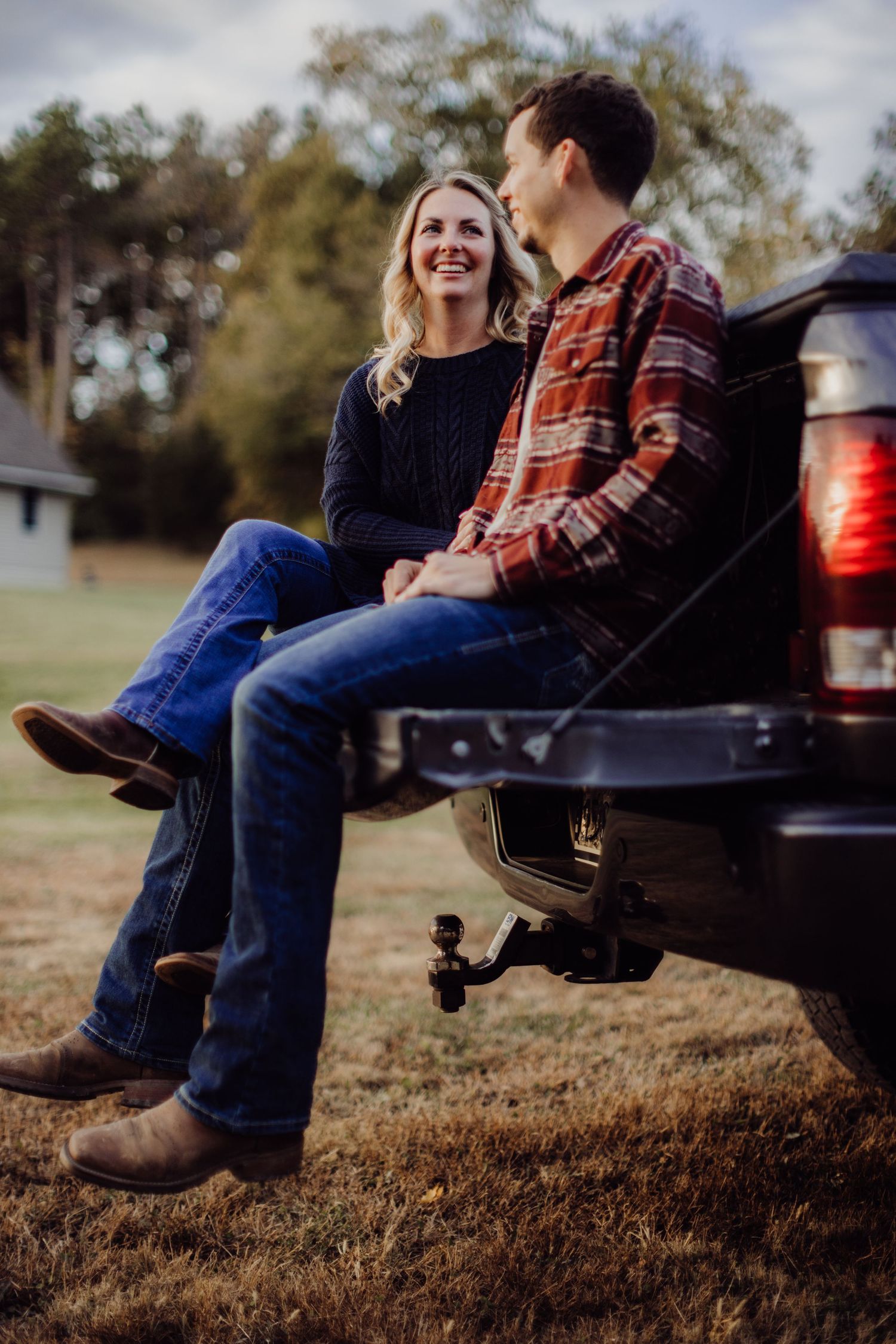 A couple shares a joyful moment while sitting on the tailgate of a pickup truck at sunset.