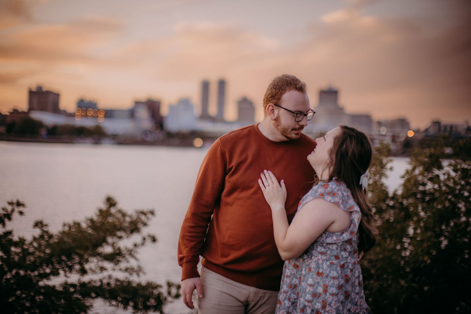 Intimate couple moment captured against city skyline and waterfront at dusk.