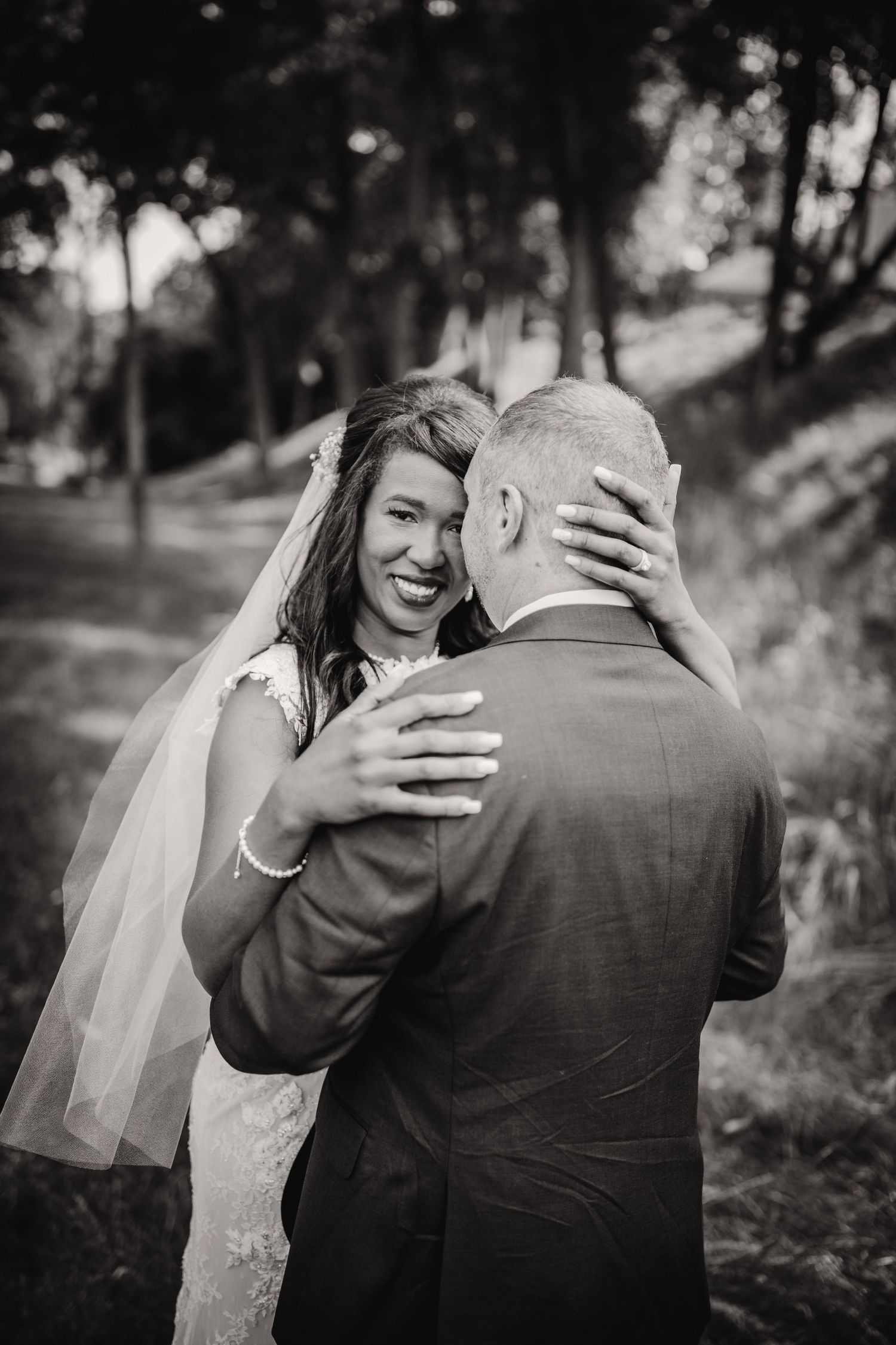 Black and white wedding photograph capturing genuine emotion and embrace in a natural outdoor setting.