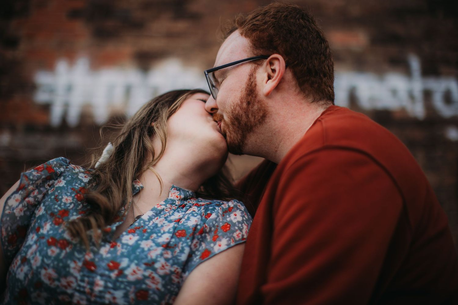 An intimate couple portrait with a floral dress and burgundy sweater creates a romantic urban scene.