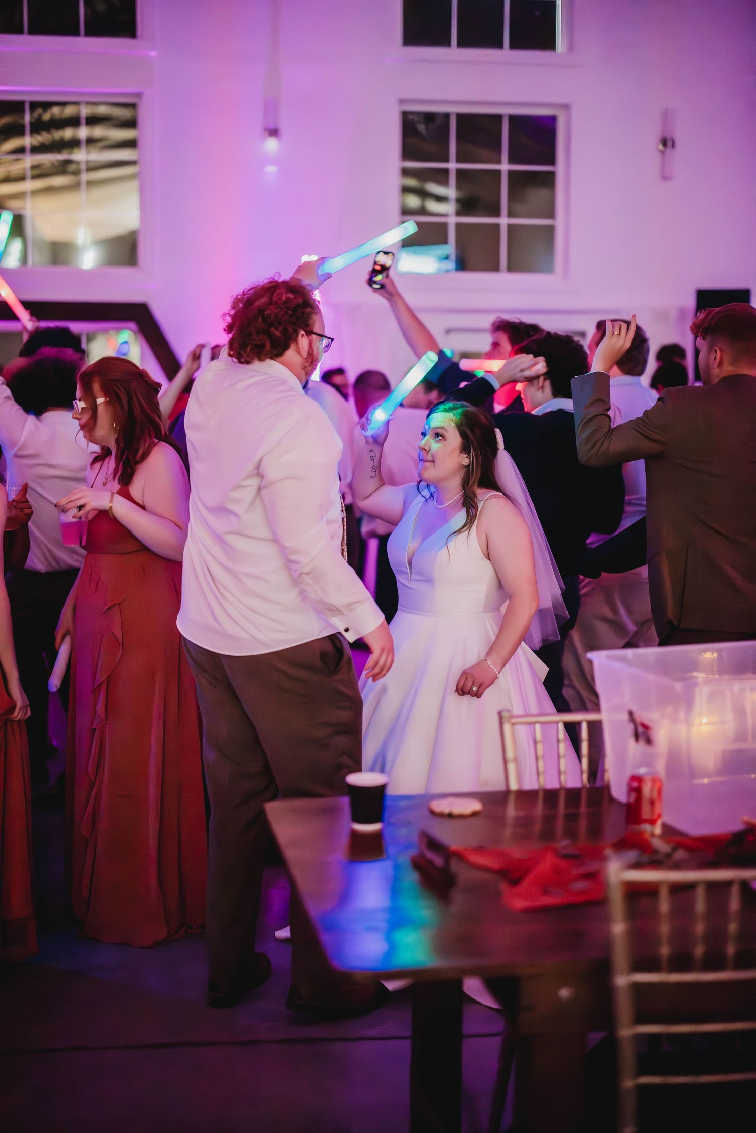 Reception guests dancing and holding light-up sticks under purple and blue mood lighting.