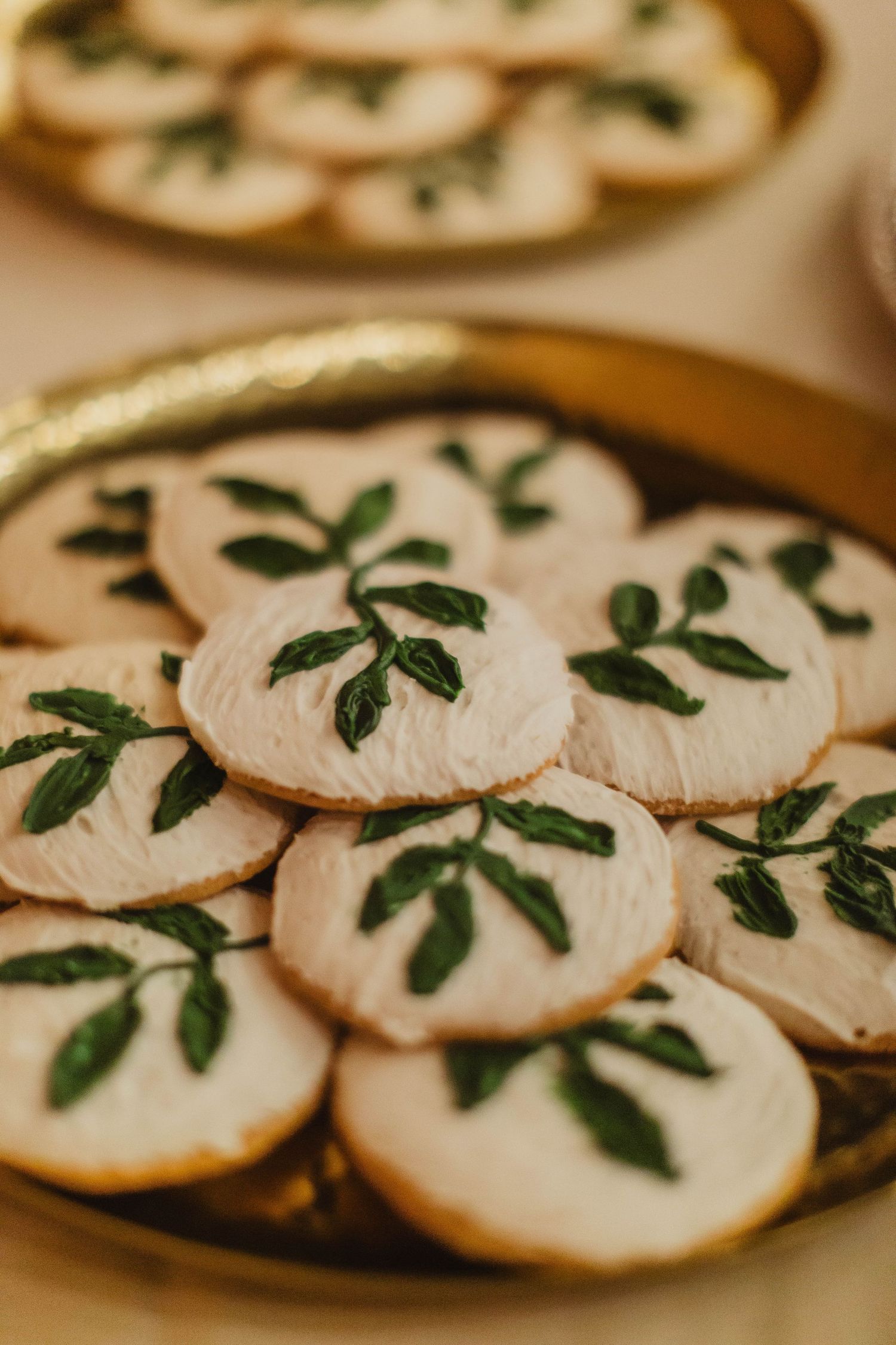 White frosted cookies decorated with green leaf designs on gold plate.