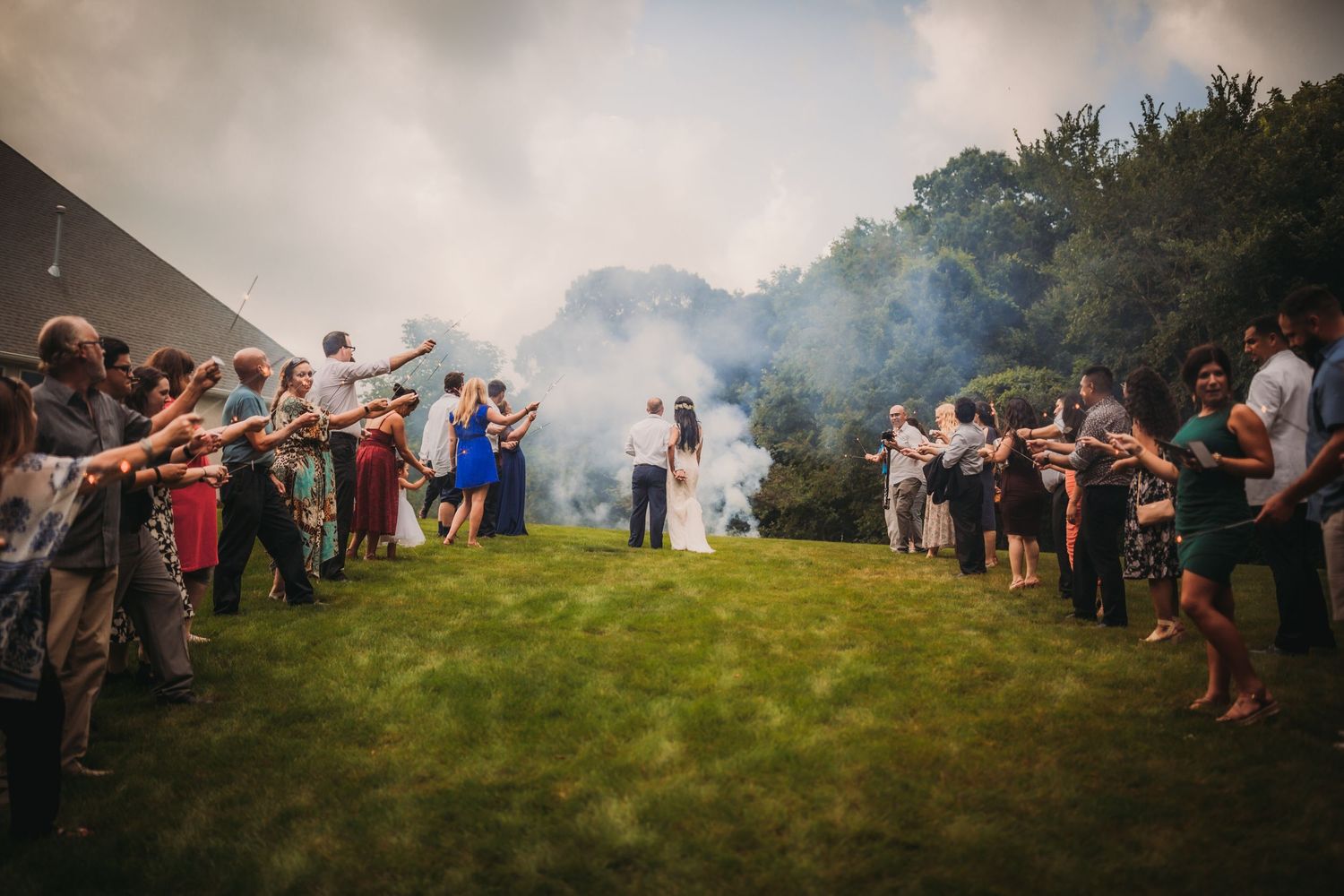 Wedding guests on a hillside create a panoramic scene with atmospheric smoke effects.
