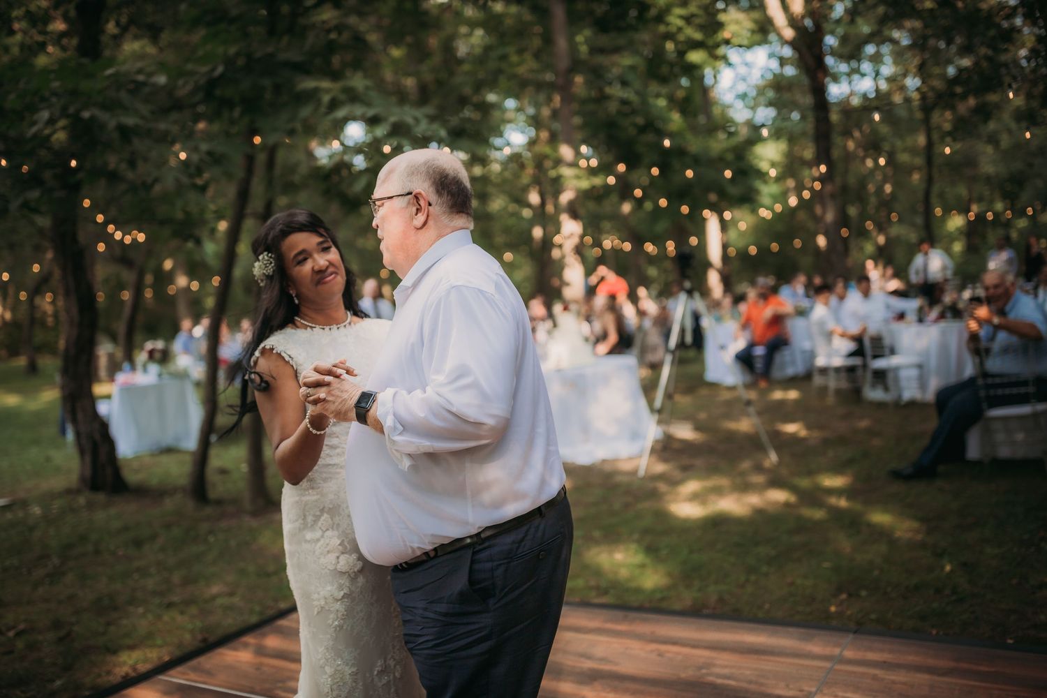 Couple shares an intimate dance on an outdoor wooden deck surrounded by trees at sunset during their wedding celebration.