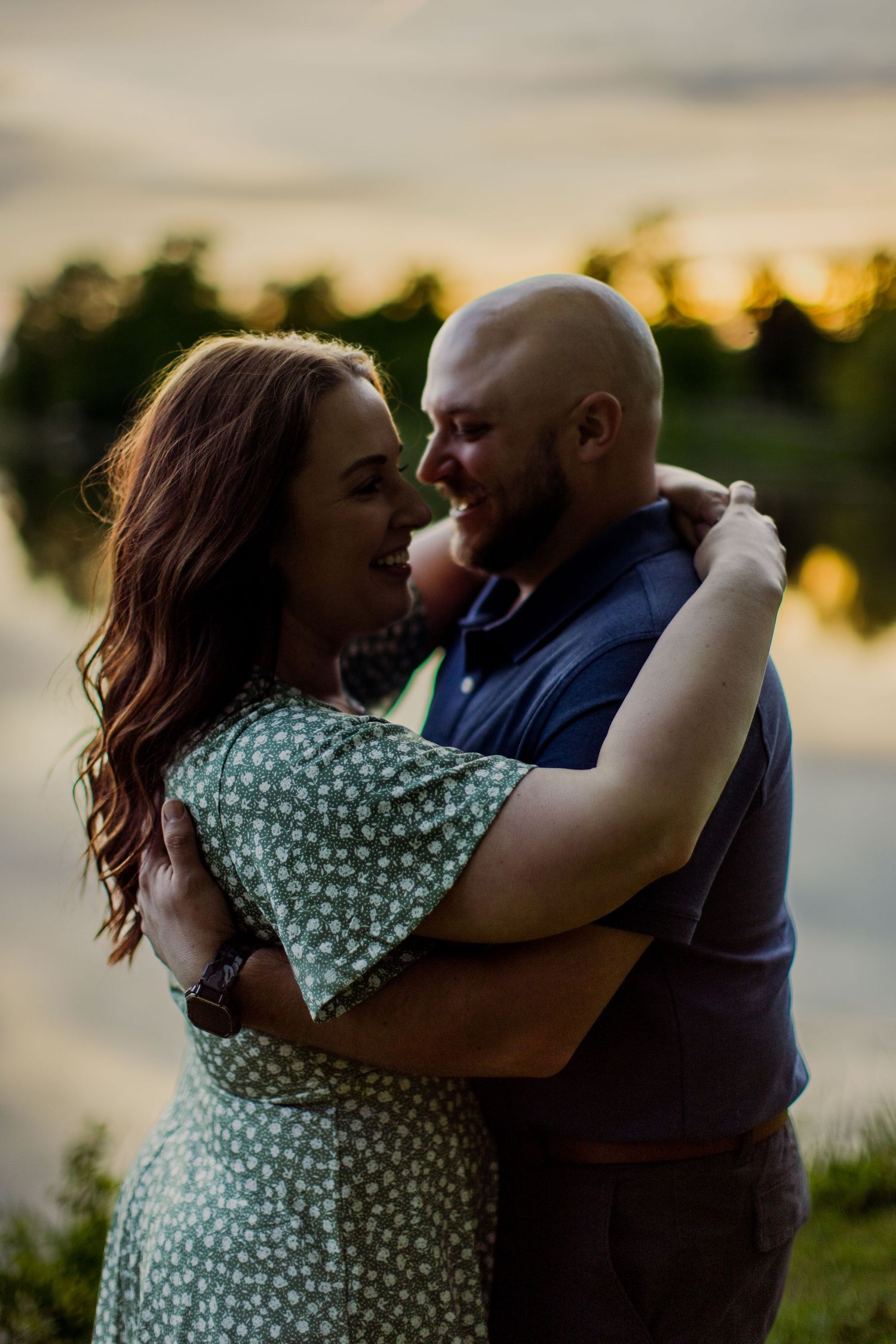 A romantic embrace between two people by a lake during sunset.
