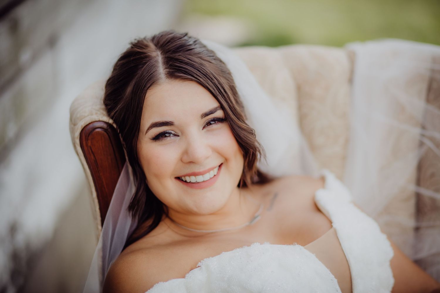 Radiant bridal portrait in classic white gown and veil against light background.