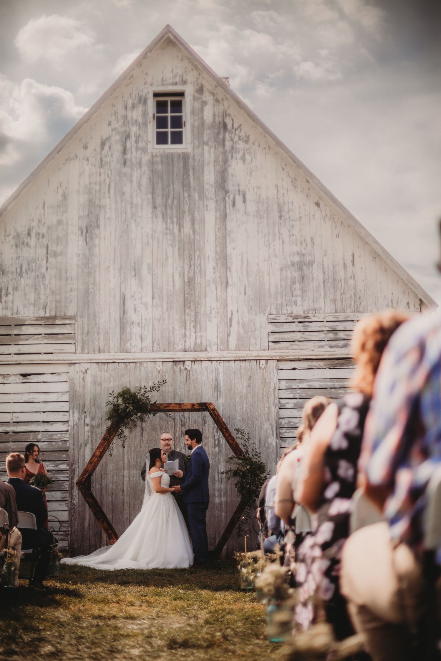 Elegant outdoor wedding ceremony in front of weathered white barn.
