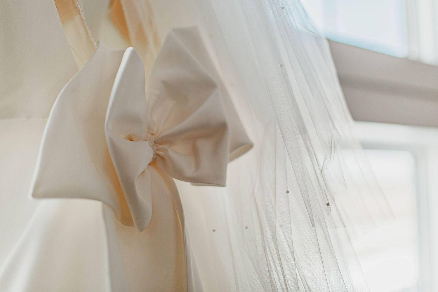 Close-up of white fabric with delicate bow detail against bright window light.