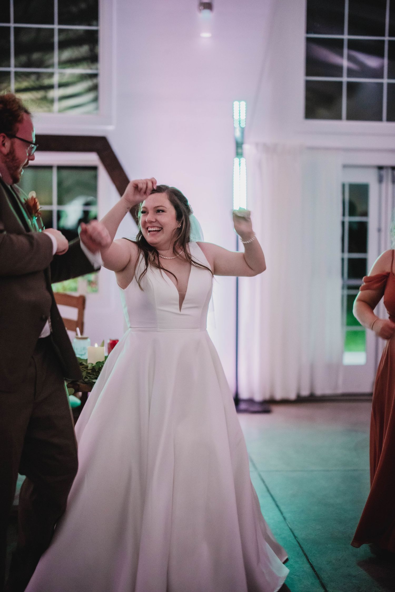 A bride in a plunging V-neck ballgown celebrates with raised arms on the dance floor.