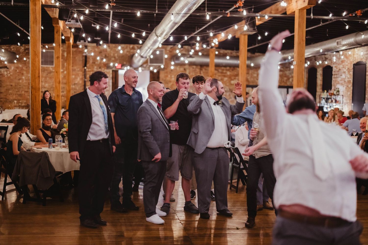 Festive dancing scene at a wedding reception in a converted barn space with ambient lighting.
