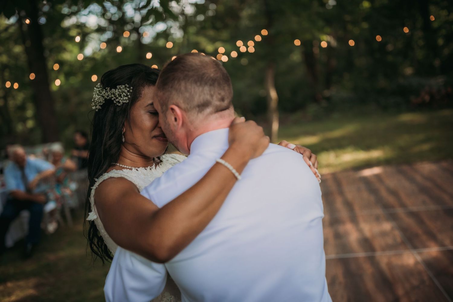 Newlyweds share an intimate dance moment at outdoor reception with twinkle lights in background.