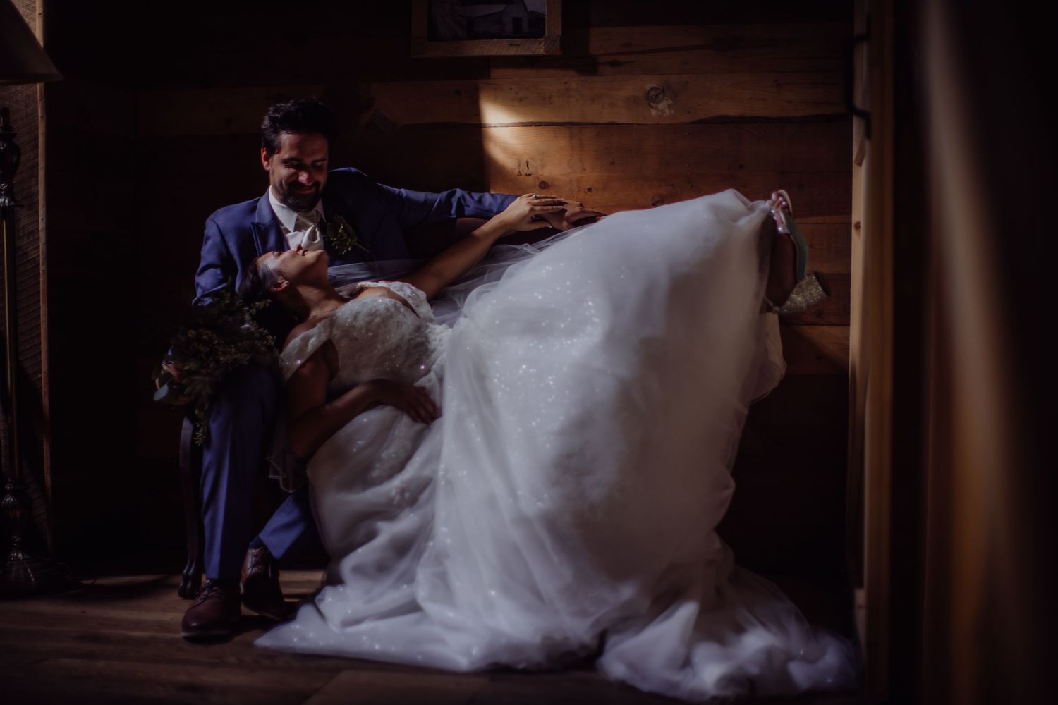 A couple in formal wedding attire share an intimate moment in moody lighting.