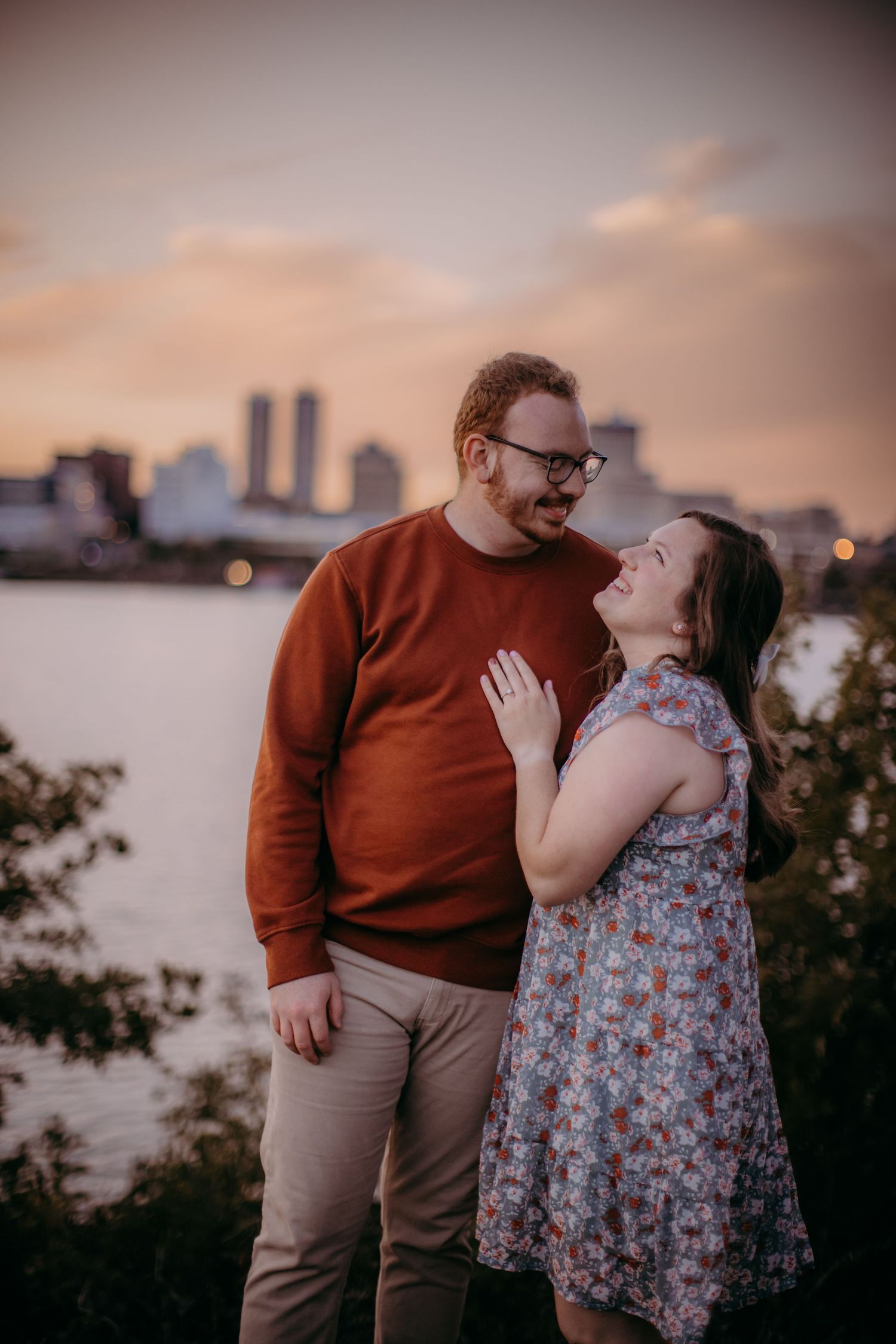Couple shares tender moment against urban waterfront backdrop during sunset.