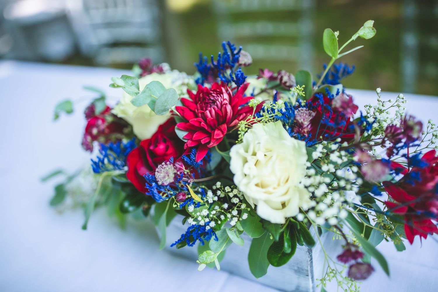 Wedding floral arrangement featuring red roses, blue delphinium, and white baby's breath.