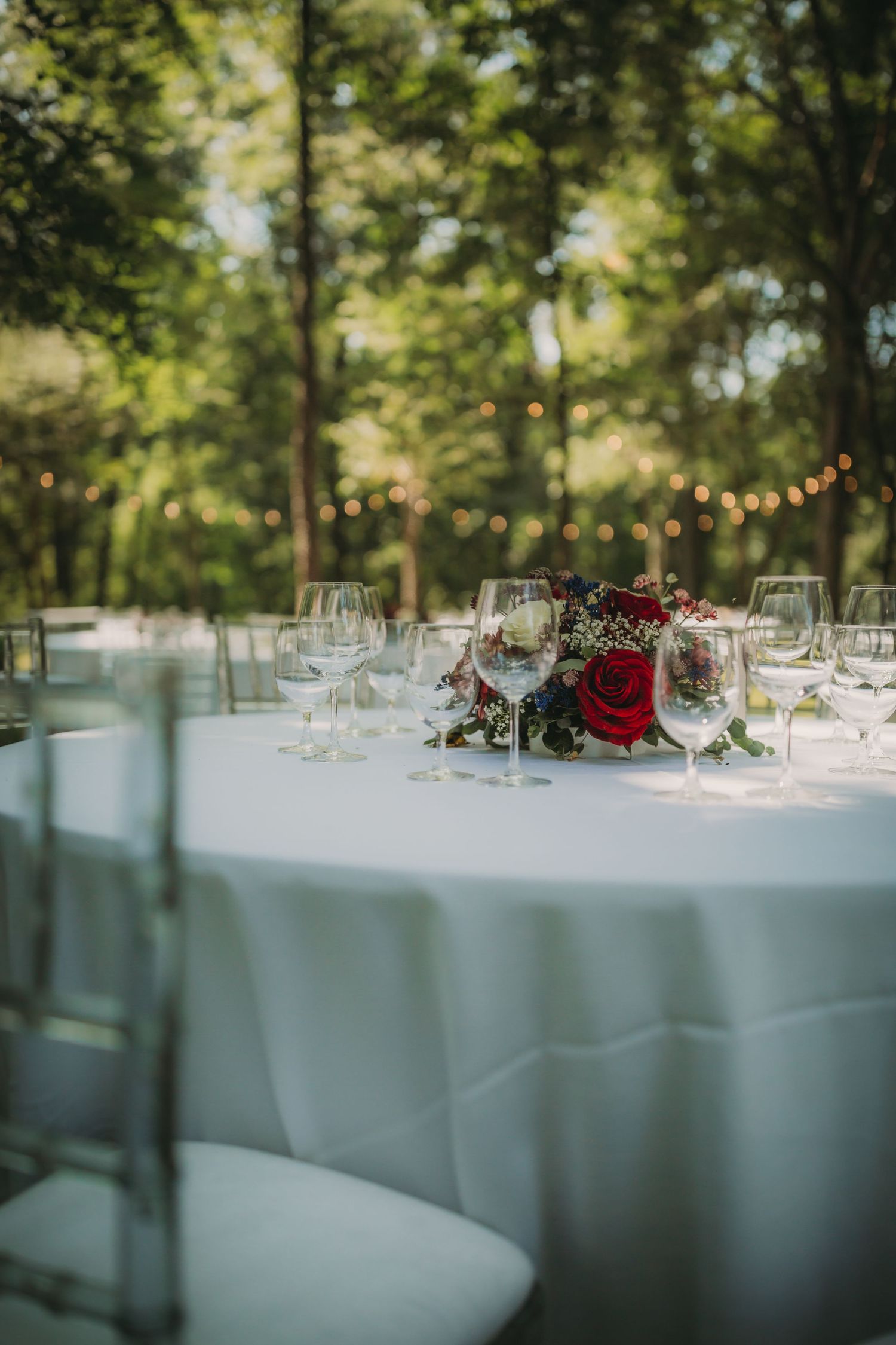 Wedding reception tables set with crystal glassware and red floral arrangements under string lights.