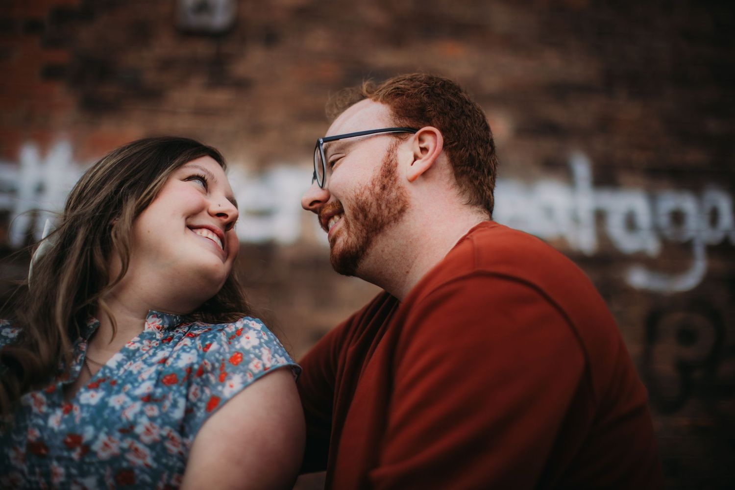 A romantic couple shares a tender moment against a brick wall backdrop during an engagement photoshoot.