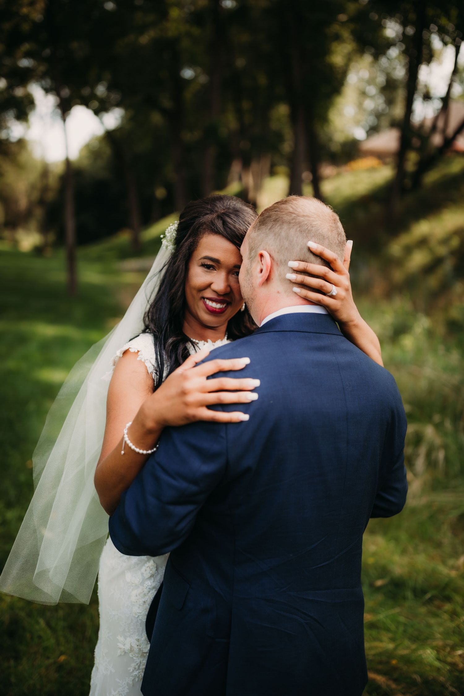 Candid wedding portrait showing joyful laughter and embrace in a sunlit forest setting.