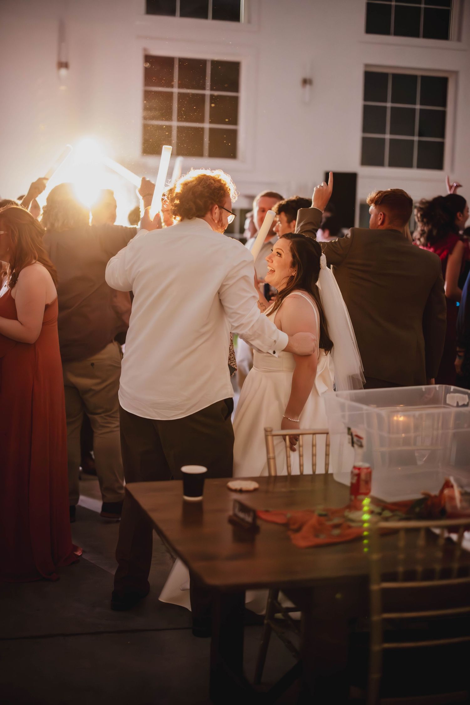 Wedding celebration with guests dancing in a bright indoor venue with high ceilings.