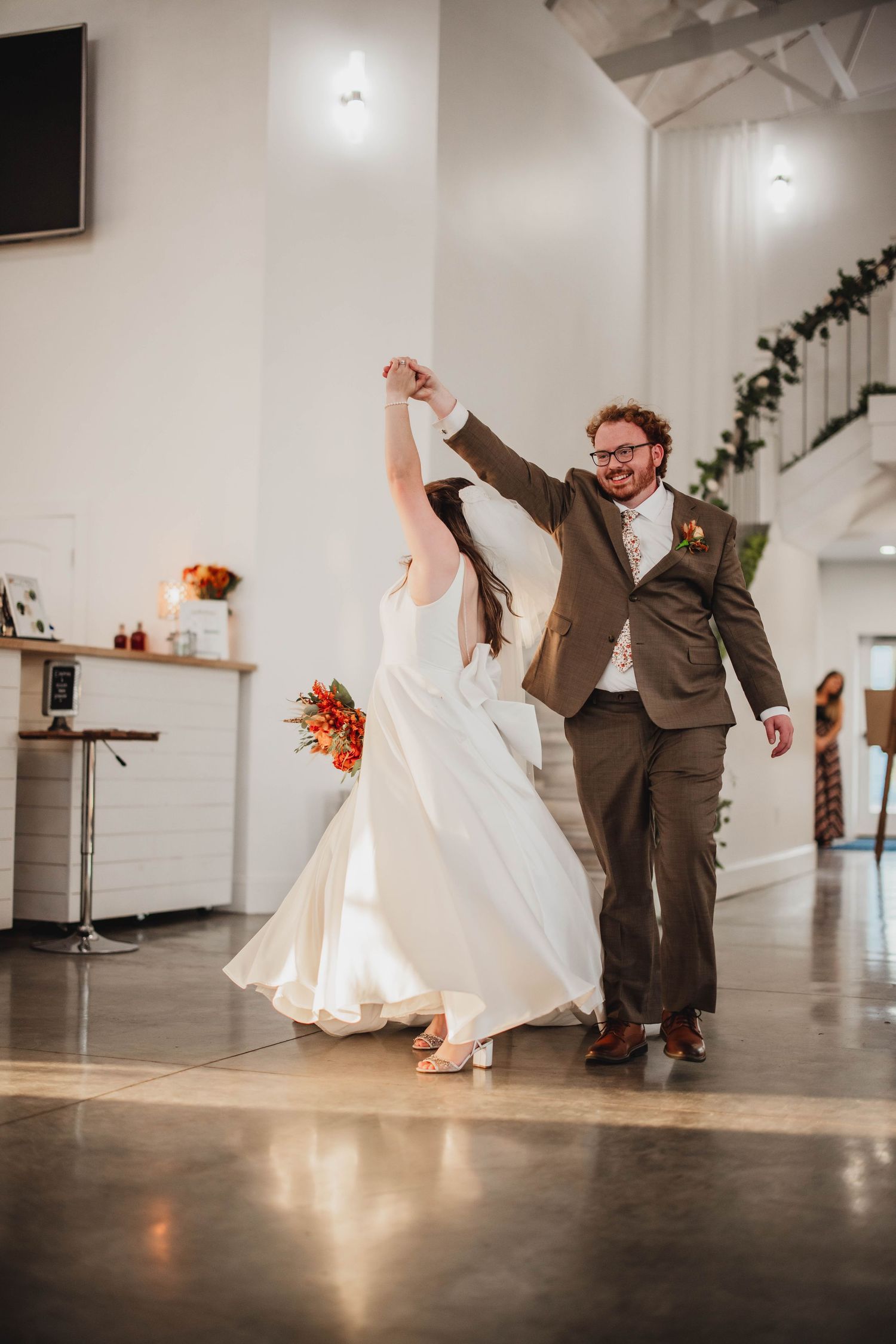 Wedding couple performs a spinning dance move in their elegant reception venue with white decor.