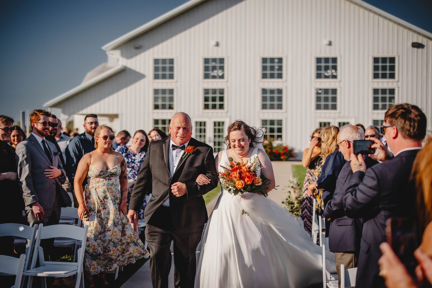 Wedding ceremony entrance at modern white barn with guests in attendance.
