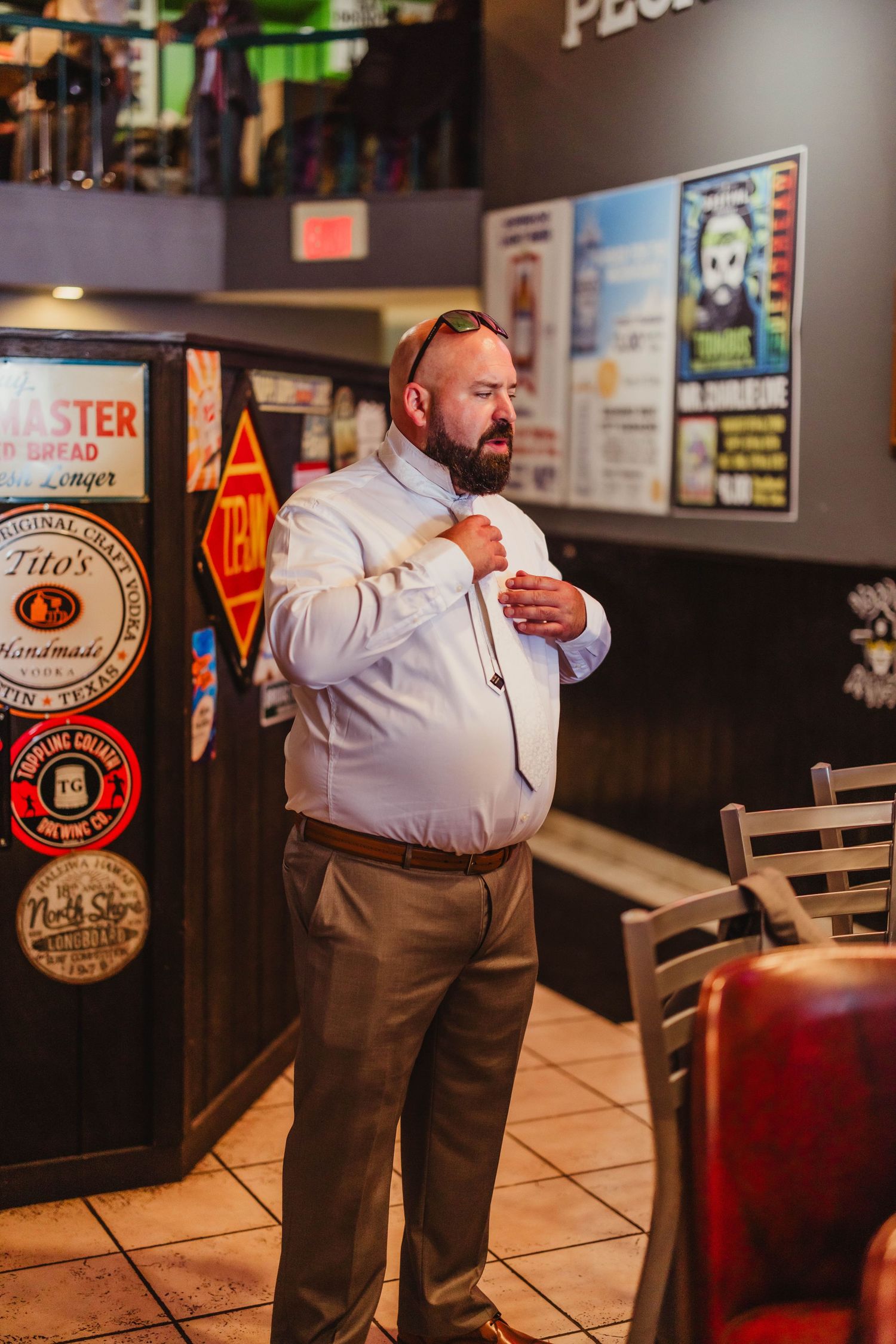 Person in white dress shirt and khakis adjusting tie in restaurant setting.