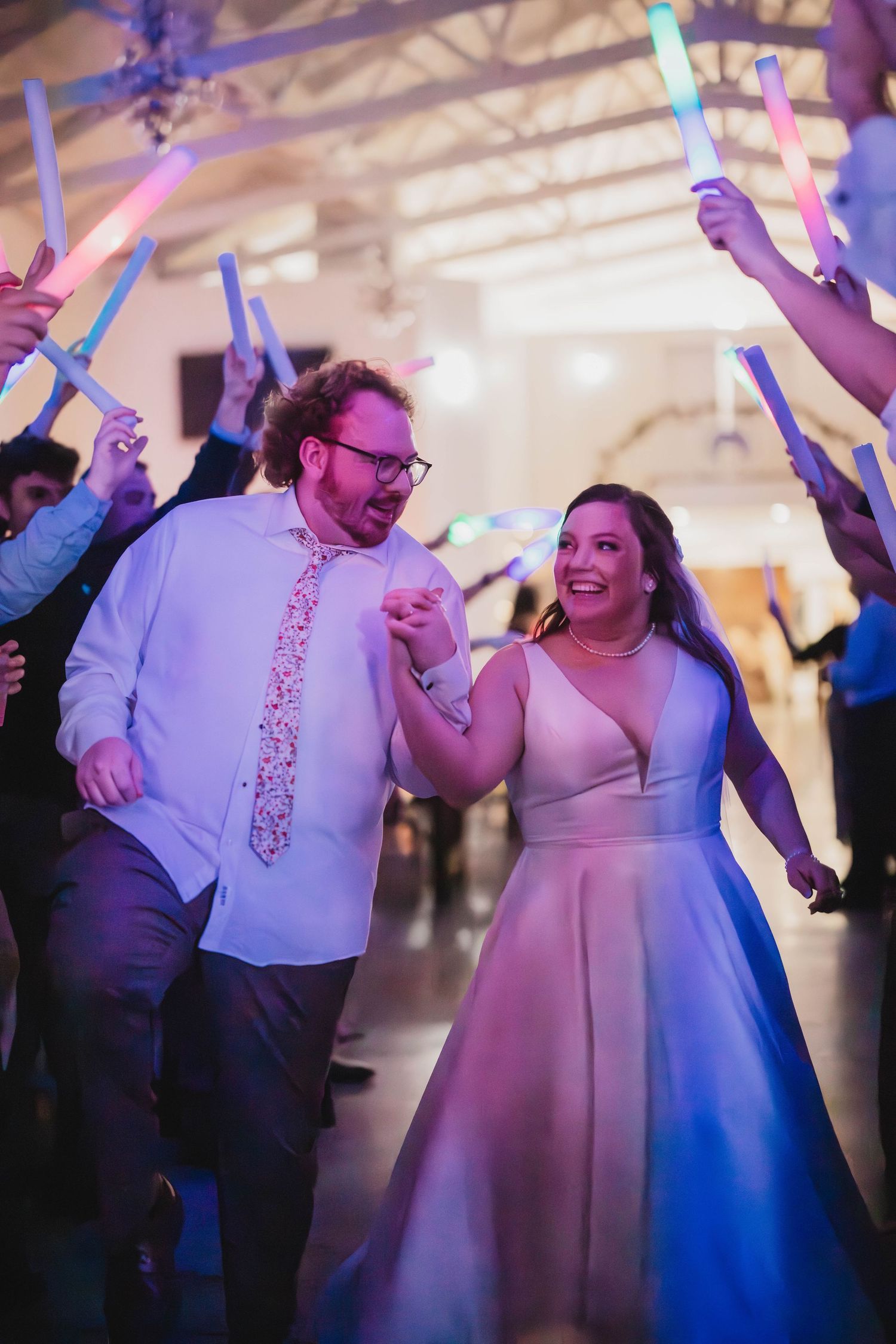 A couple dances joyfully at their wedding reception while guests wave colorful LED light sticks in celebration.
