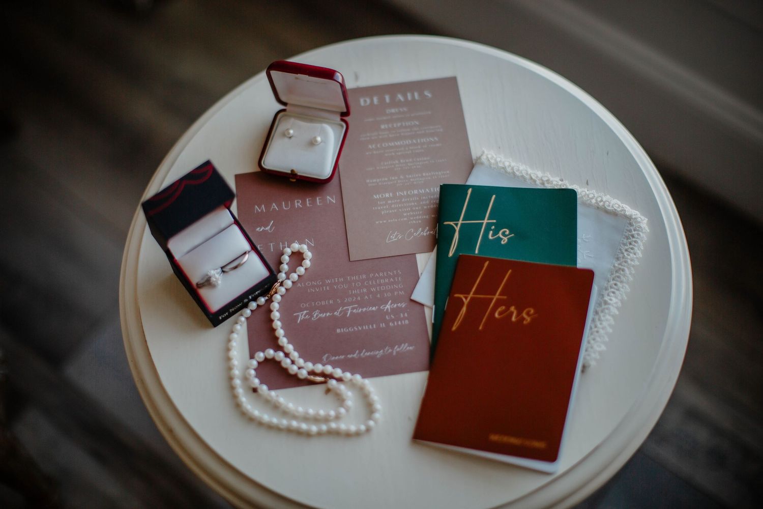 Wedding invitations and pearl necklace arranged on a white plate with burgundy and teal accents.
